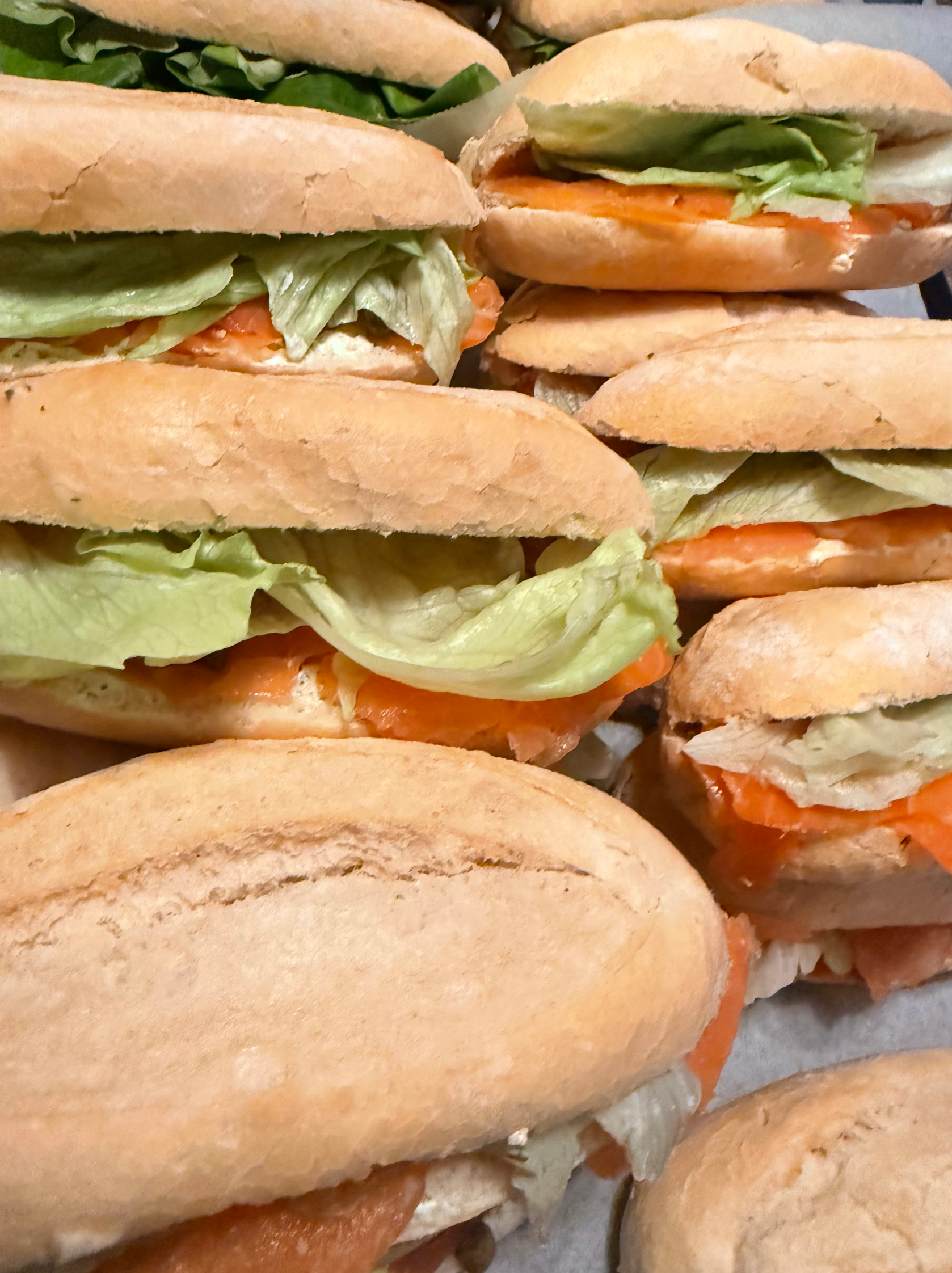 Sandwiches met sla en zalm op een lichtbruin broodje, op elkaar gestapeld.
