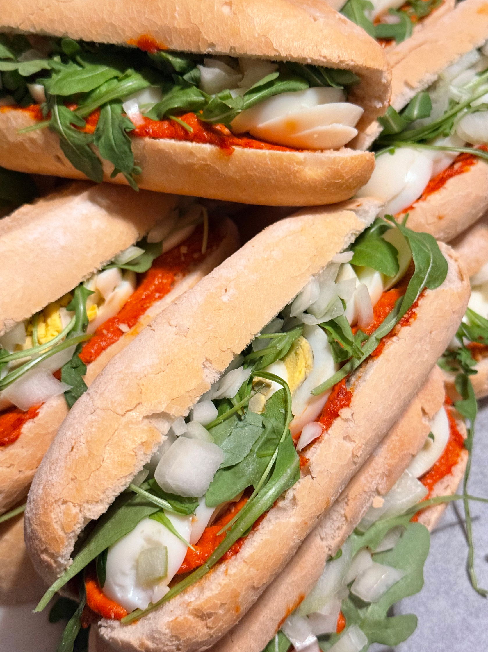Een stapel sandwiches met rucola, eieren en rode saus.