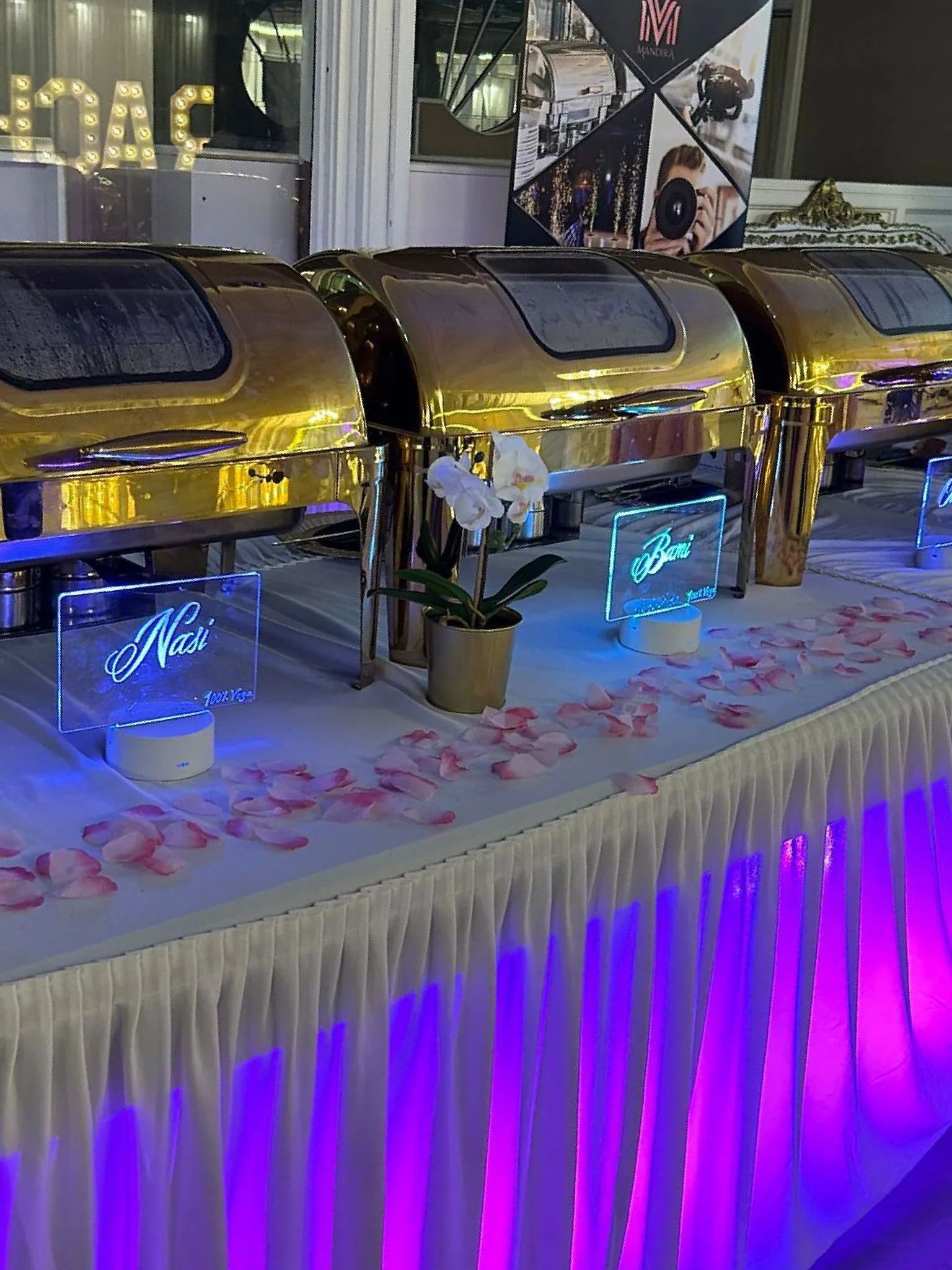 Een buffettafel met paarse lichten en gouden chafing dishes.