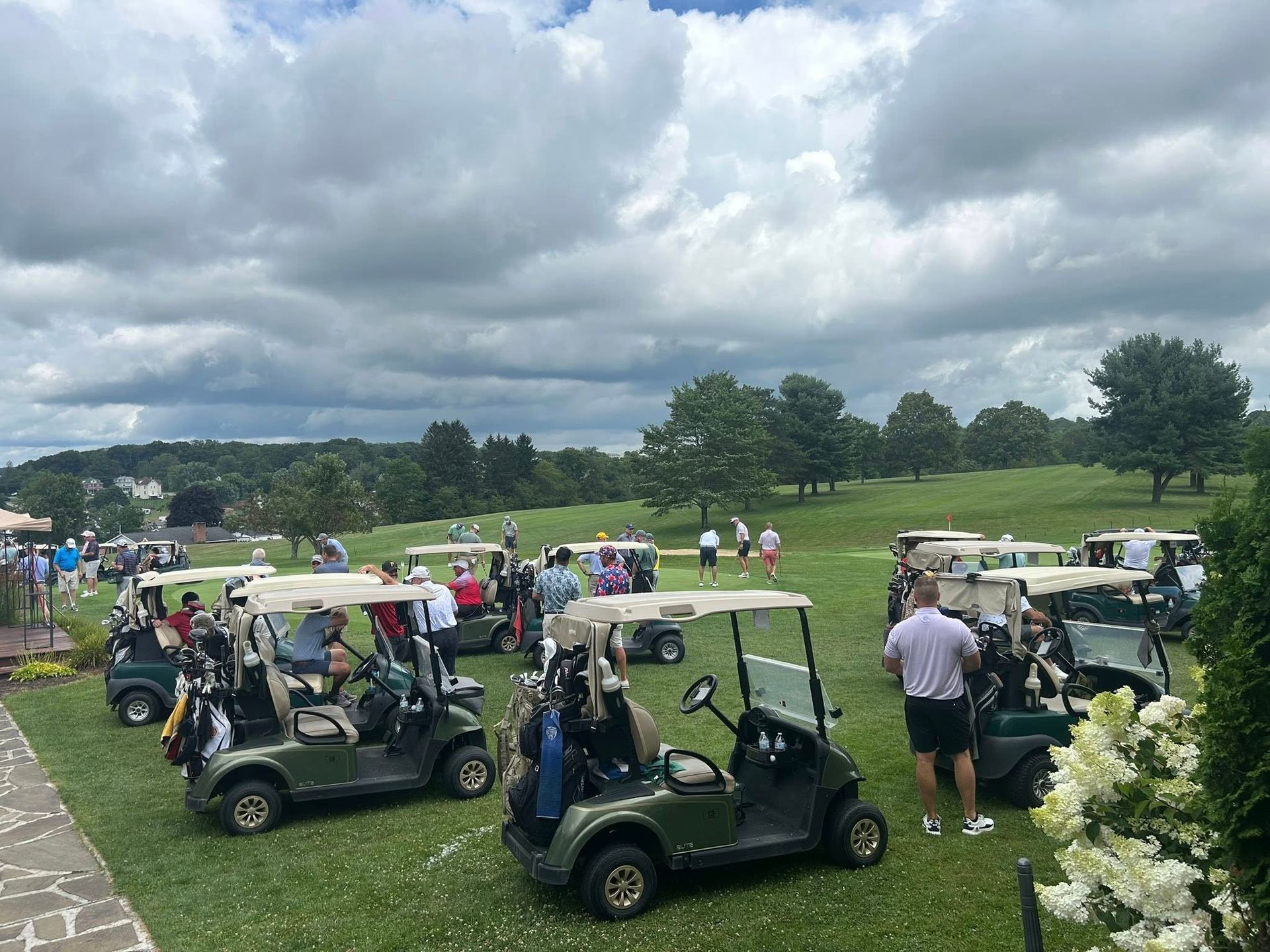 Golfers with golf carts on a grassy golf course under a cloudy sky.