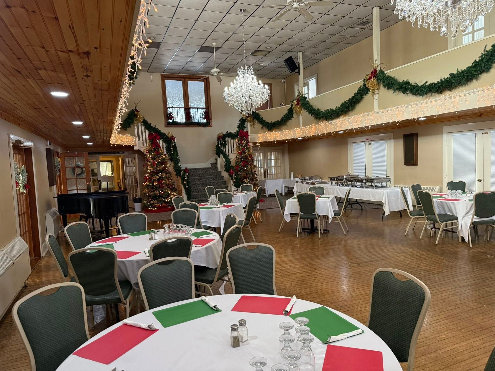 An indoor banquet hall decorated for the holidays, featuring round tables with festive place settings and chandeliers.
