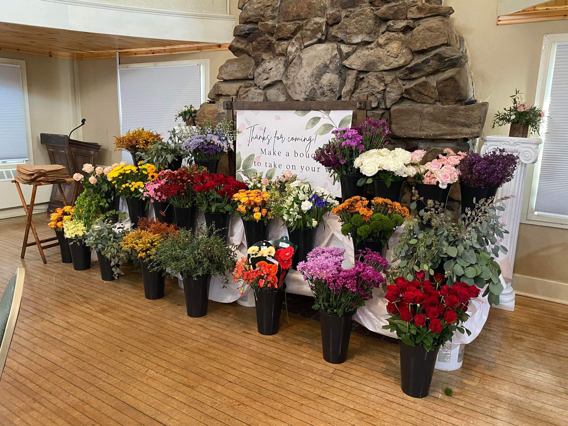 A variety of colorful flower bouquets arranged in vases on a table in front of a stone fireplace.