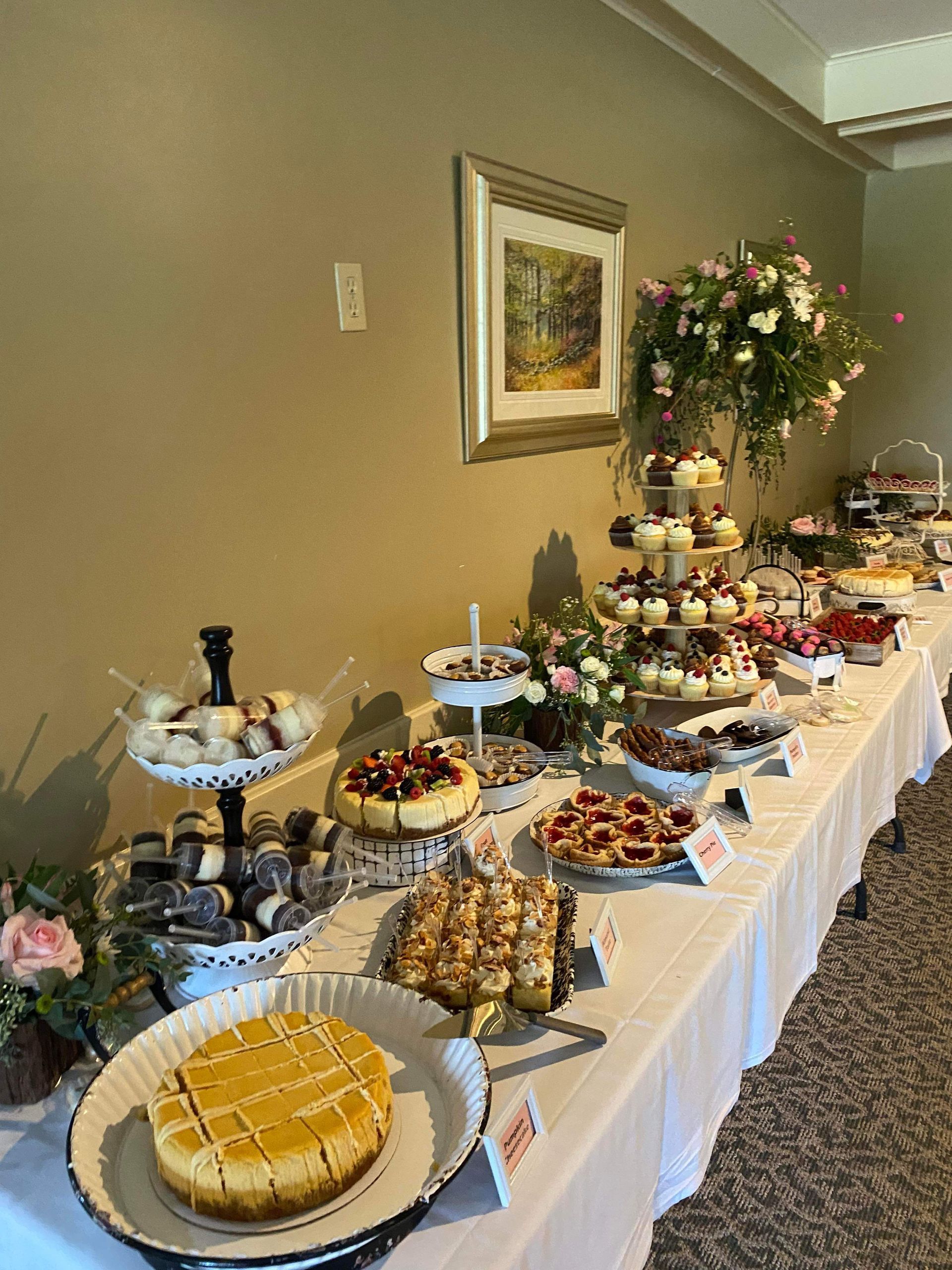 A long buffet table laden with an assortment of cheesecakes, pastries, and tiered desserts in a well-lit event room.