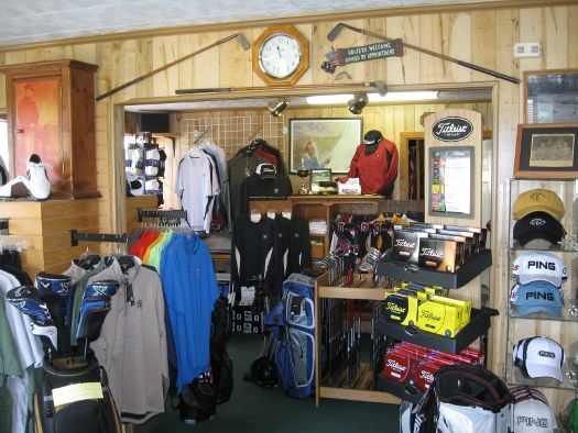 Golf shop interior with clothing, golf bags, equipment, and a person behind the counter.