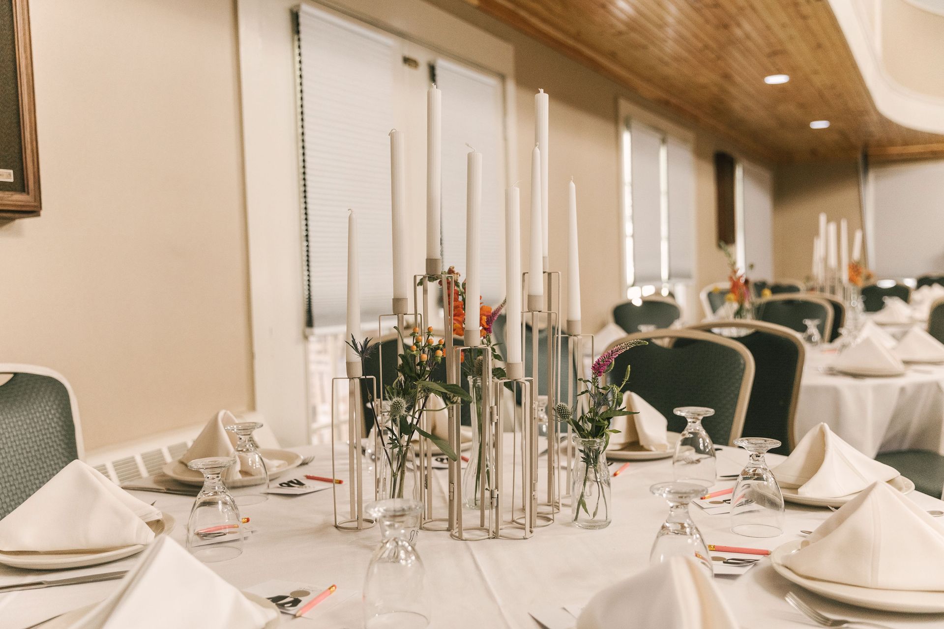Elegant dining room set for an event; round tables with white linens, gold chargers, green chairs, and floral centerpieces.