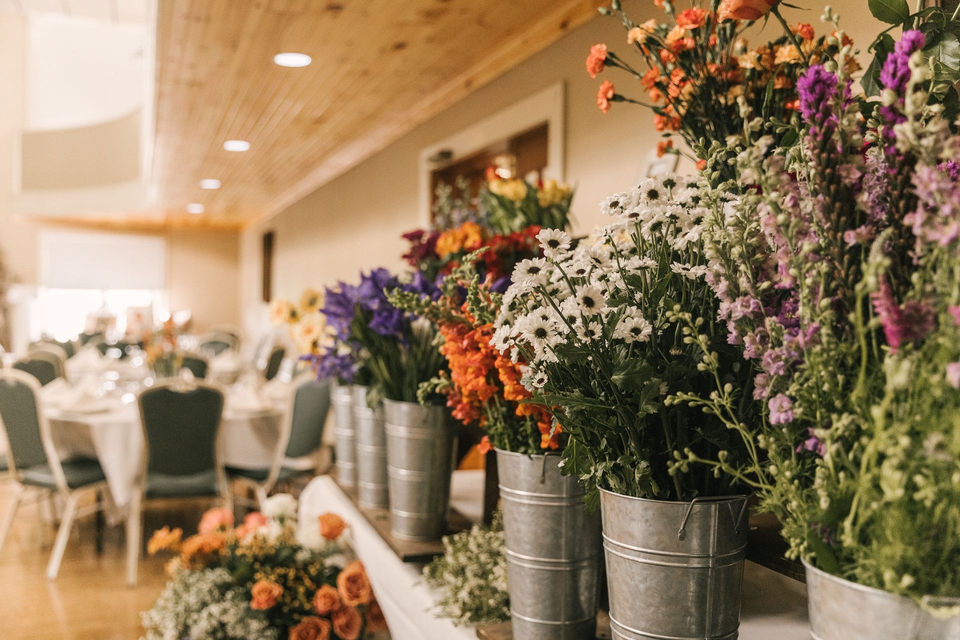 Large room with people seated at round tables; chandelier, upper balcony, and decorations.