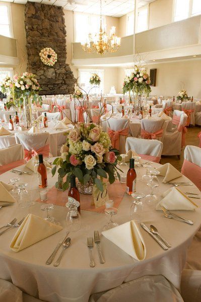 A round table at a wedding reception set with floral centerpieces, white linens, and peach-colored chair sashes.