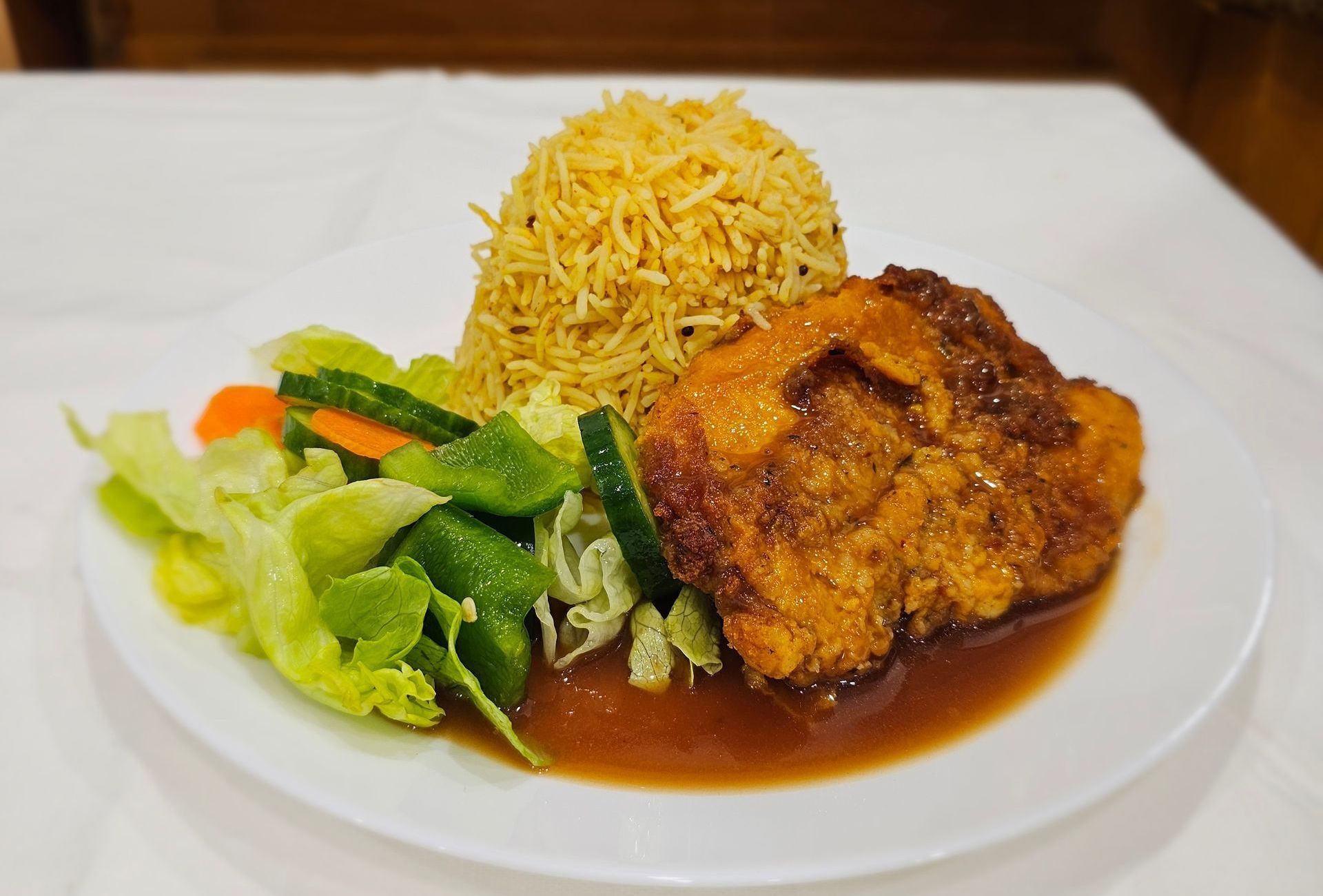 Plate with fried chicken in sauce, yellow rice, and salad.