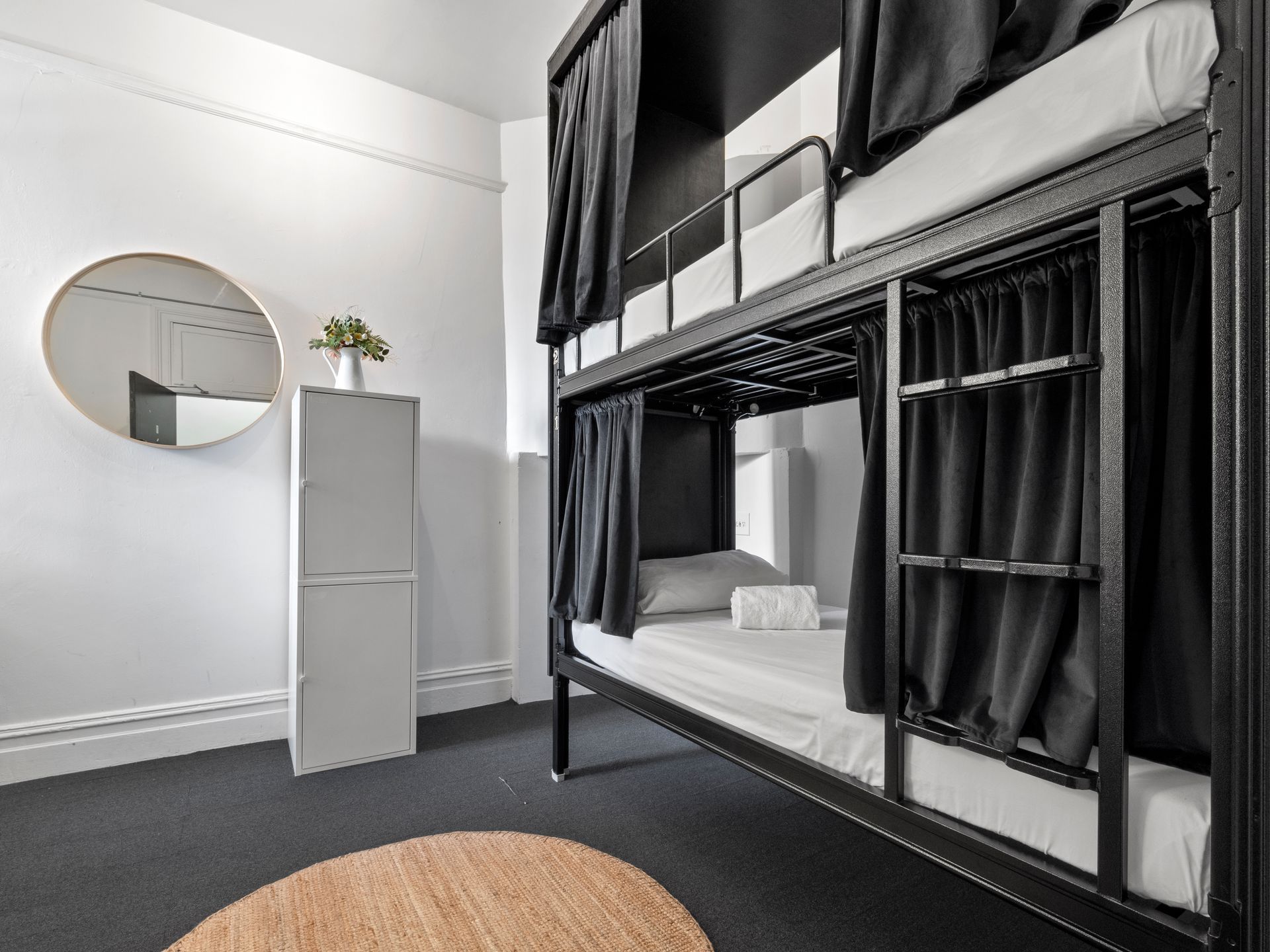 A bunk bed with black curtains and a round mirror in a room.