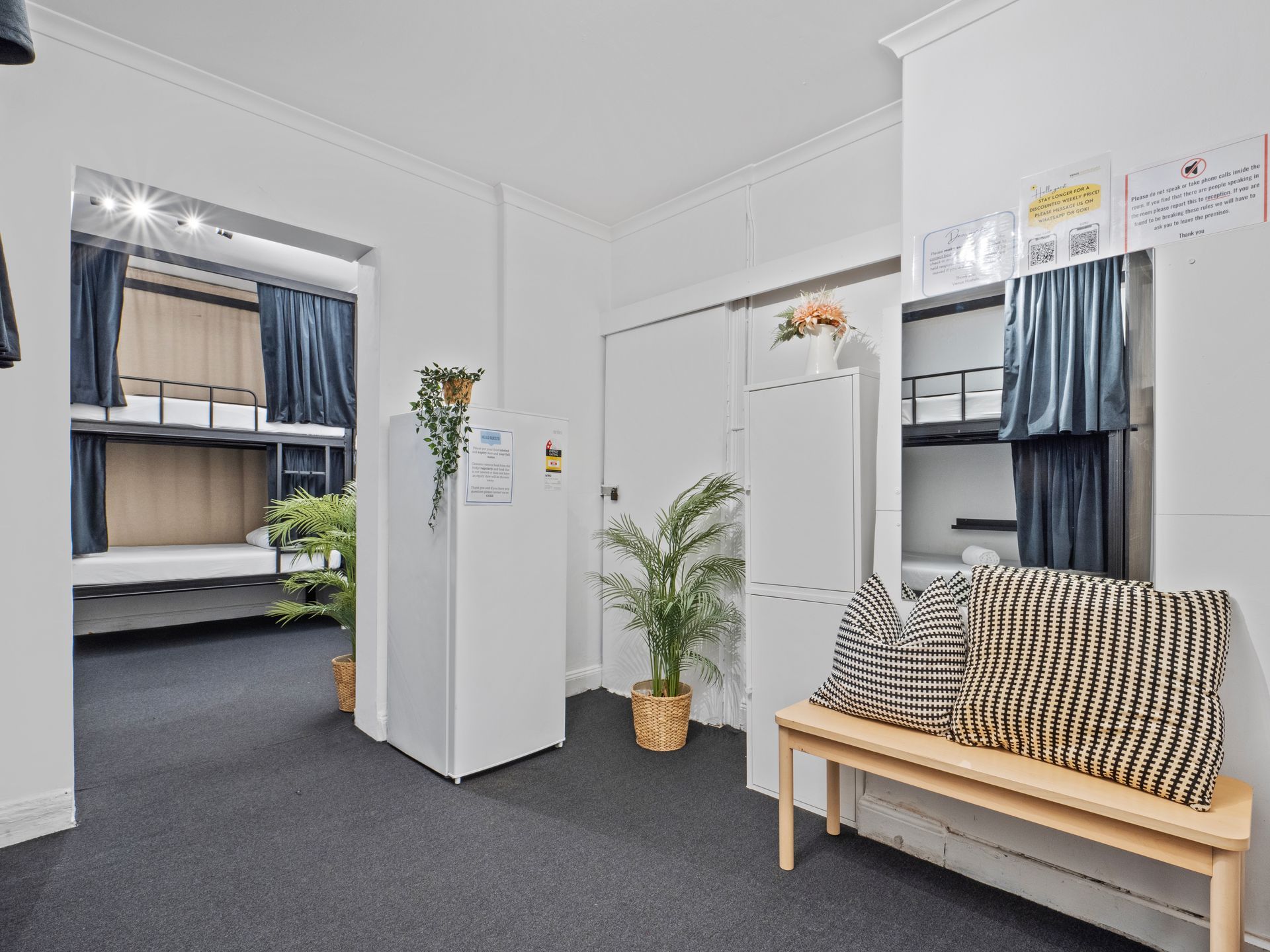 A room with bunk beds , a bench , and a refrigerator.