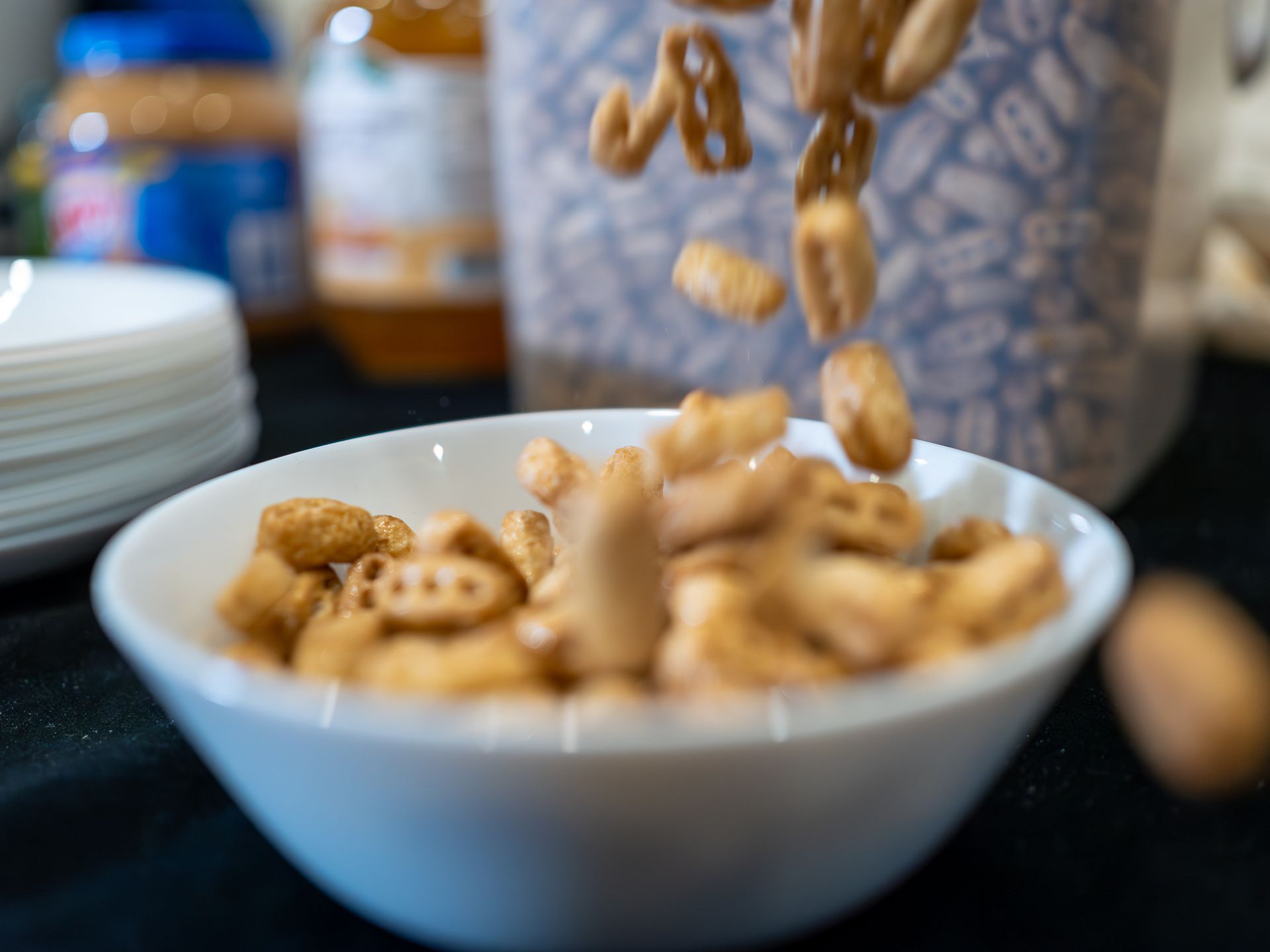 Peanuts are falling into a bowl of cereal on a table.