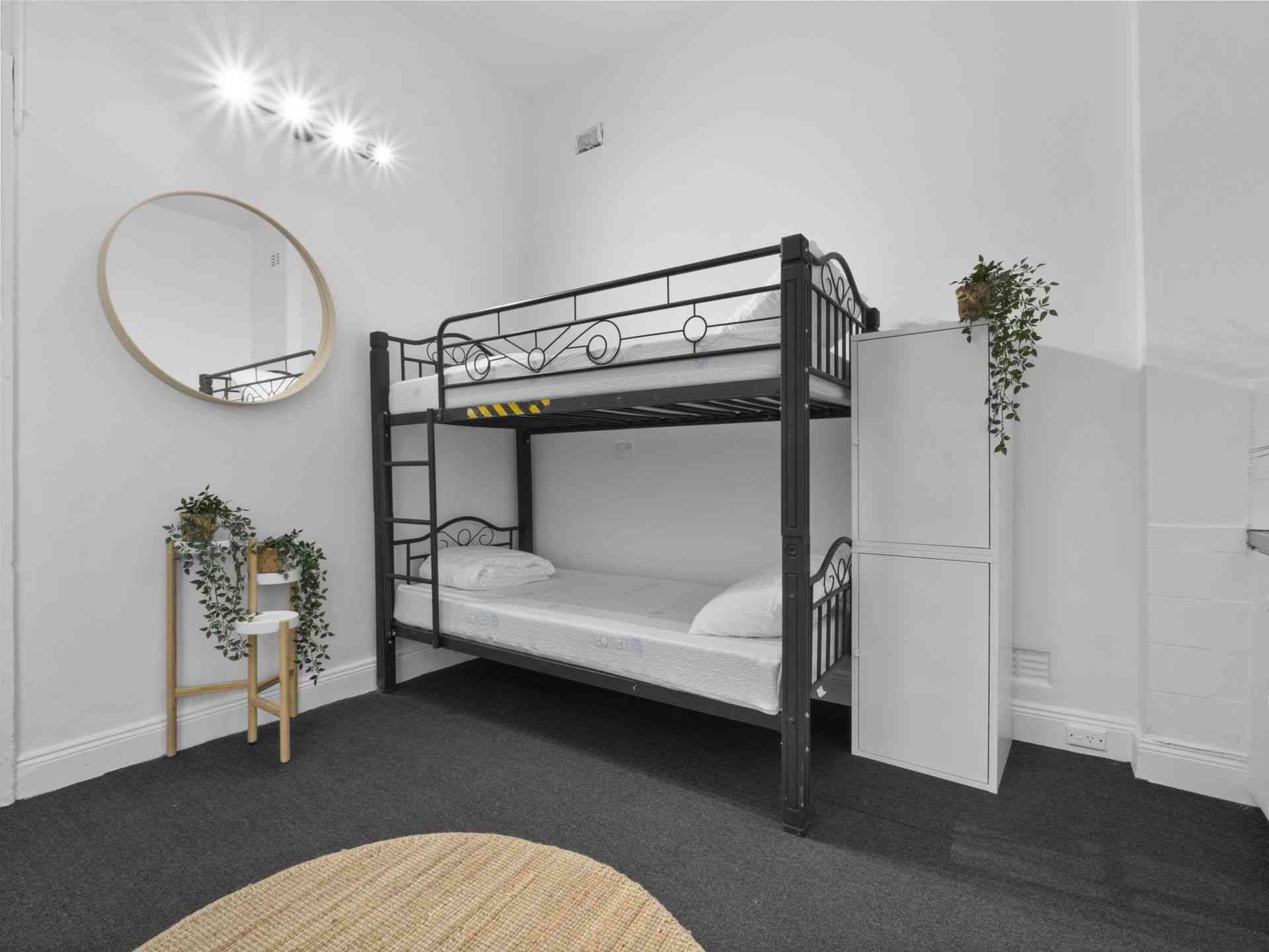 A small room with a black bunk bed, round mirror, and white storage.