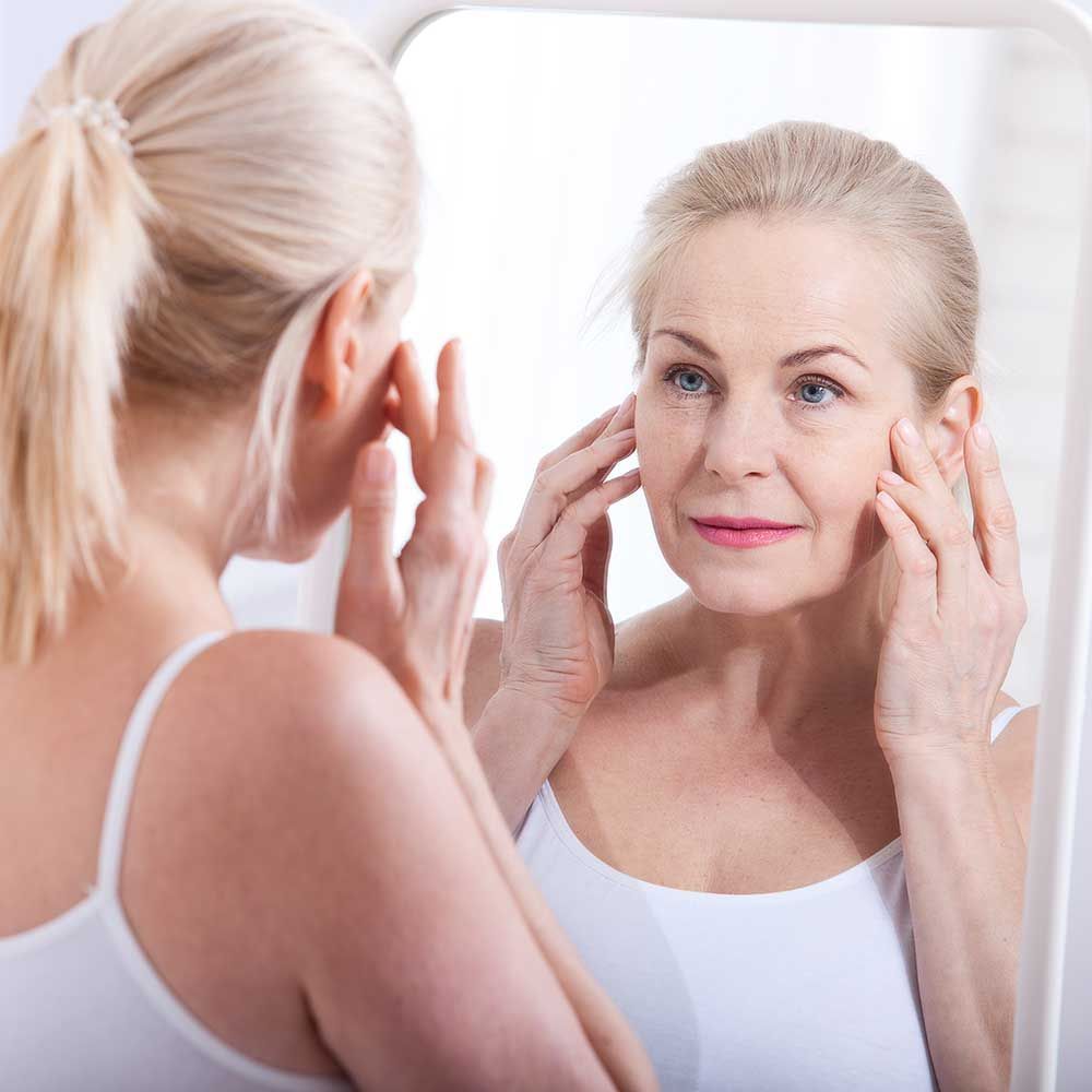 Middle aged woman looking at wrinkles in mirror