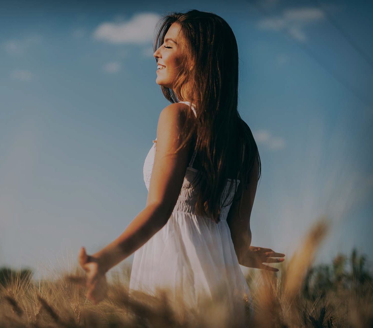 A woman in a white dress is standing in a field of wheat.