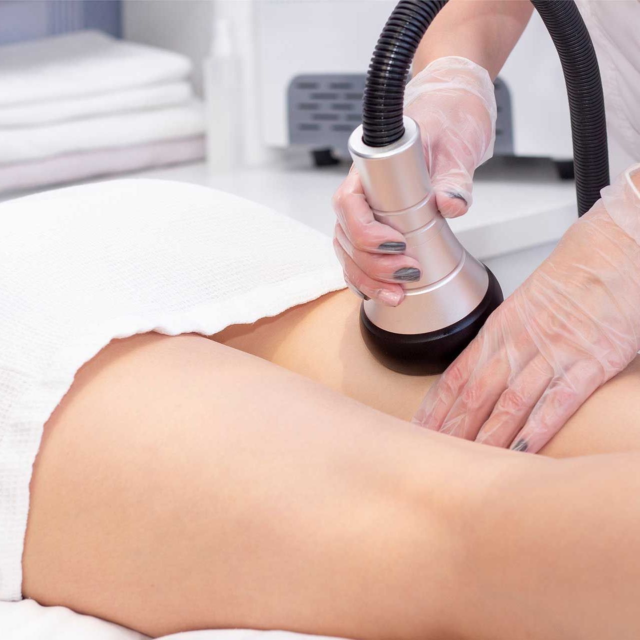 Cosmetologist reducing cellulite on hips of female patient, using ultrasound cavitation machine.