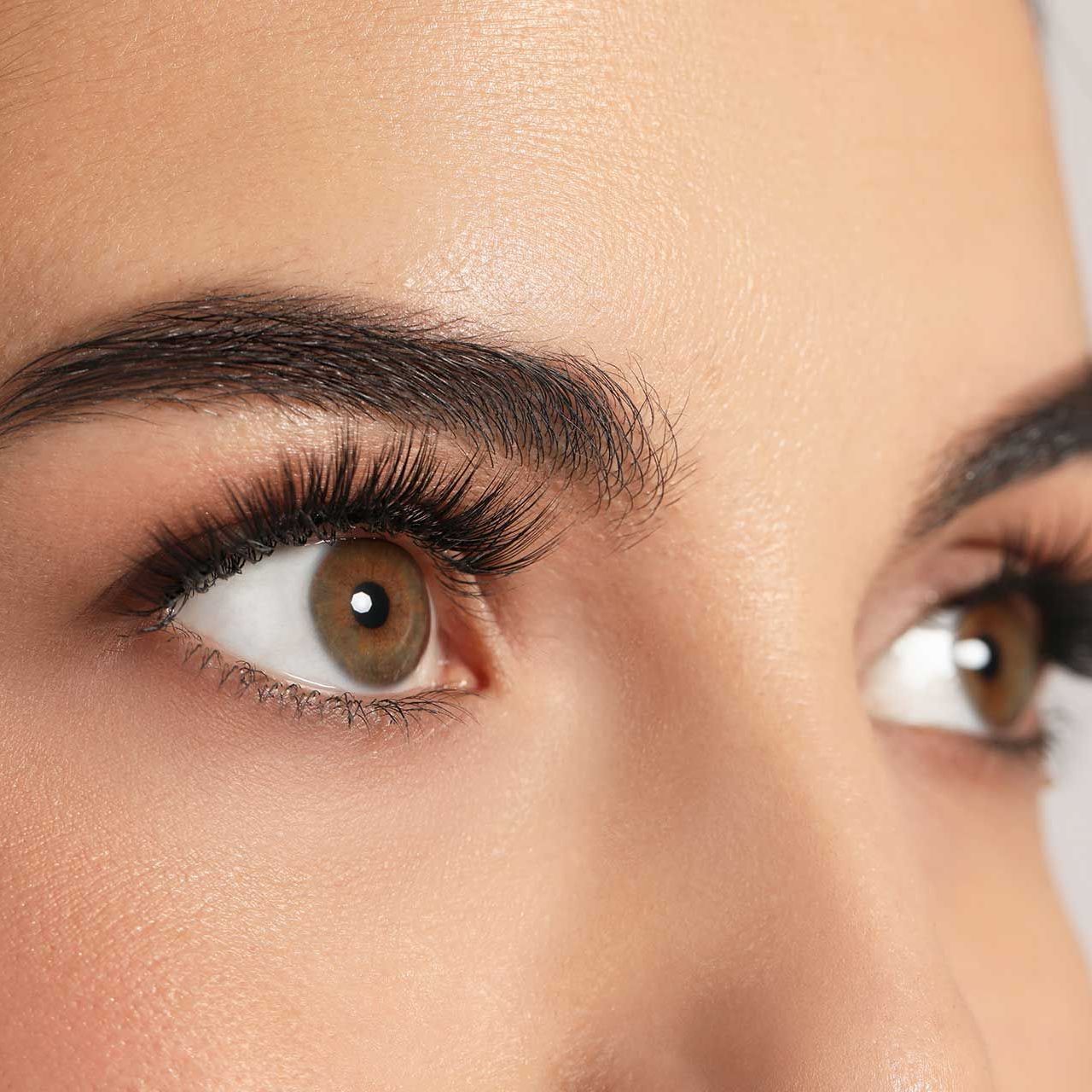Beautiful young woman with long eyelashes on light background, closeup