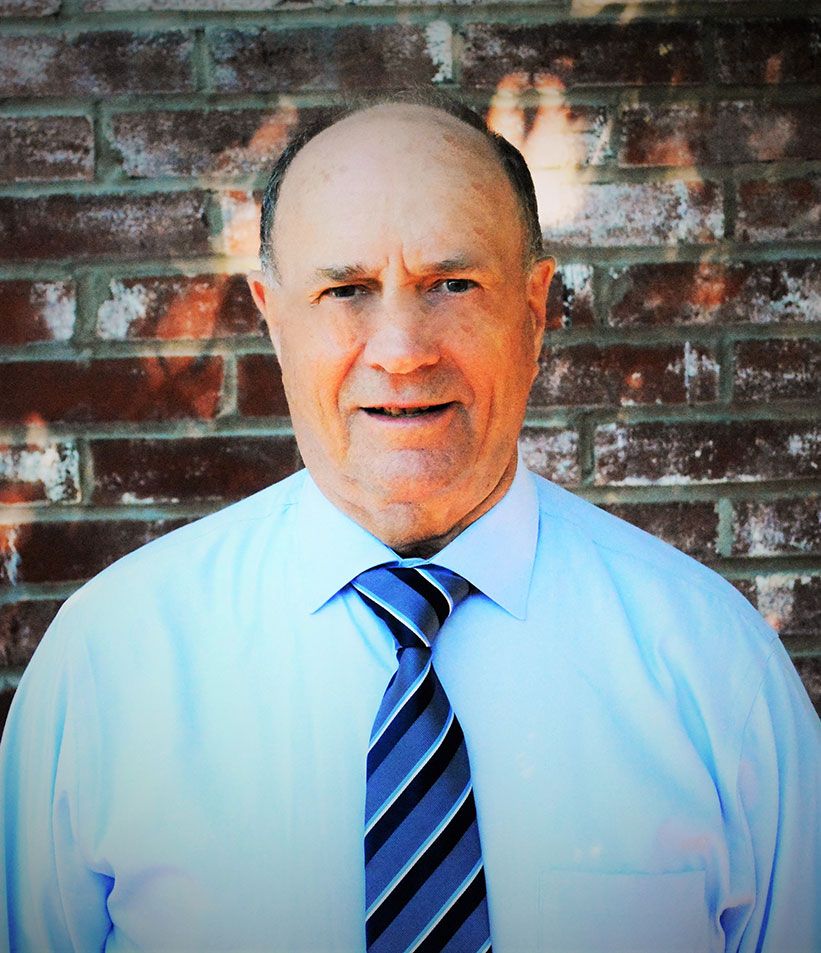 A man in a blue shirt and tie is standing in front of a brick wall