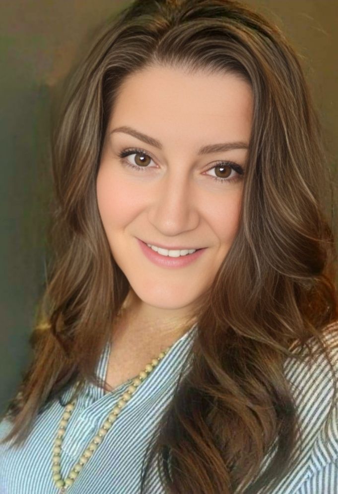 A woman with long brown hair is smiling for the camera while wearing a striped shirt and a necklace.