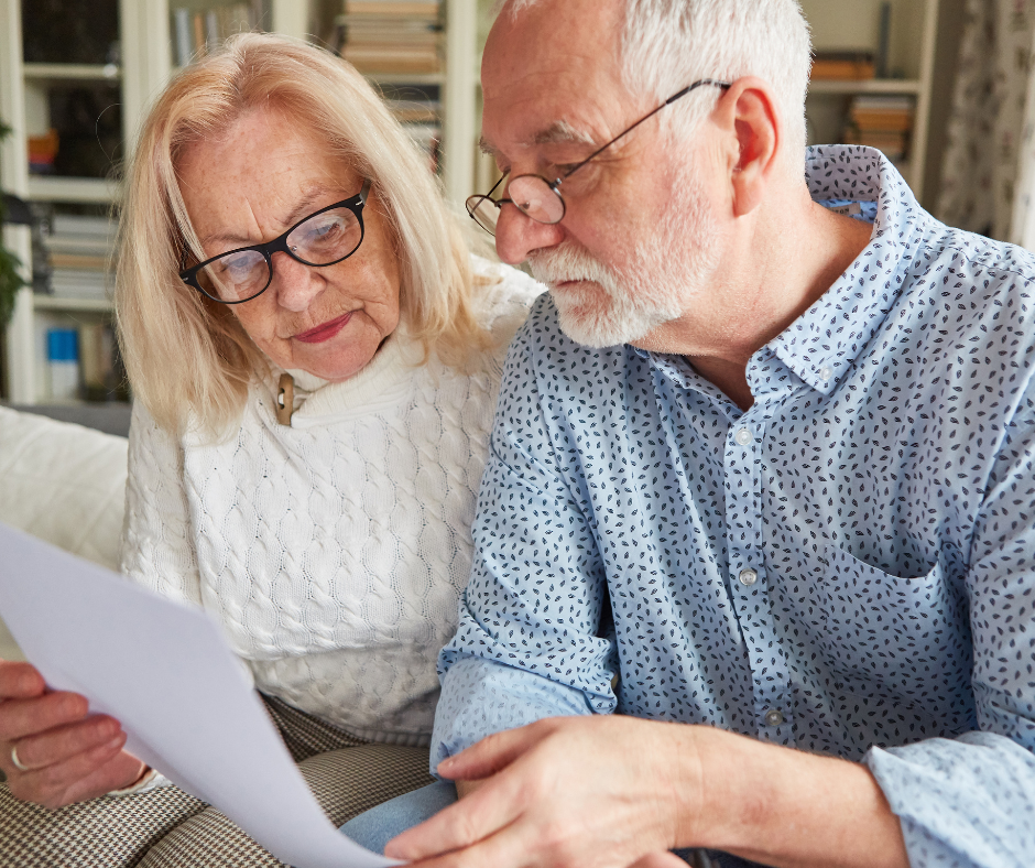 An elderly couple is sitting on a couch looking at a piece of paper.