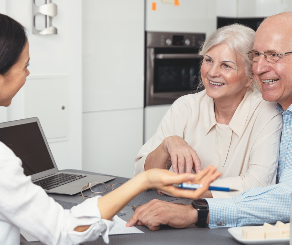 A man and woman are sitting at a table talking to a woman in front of a laptop.