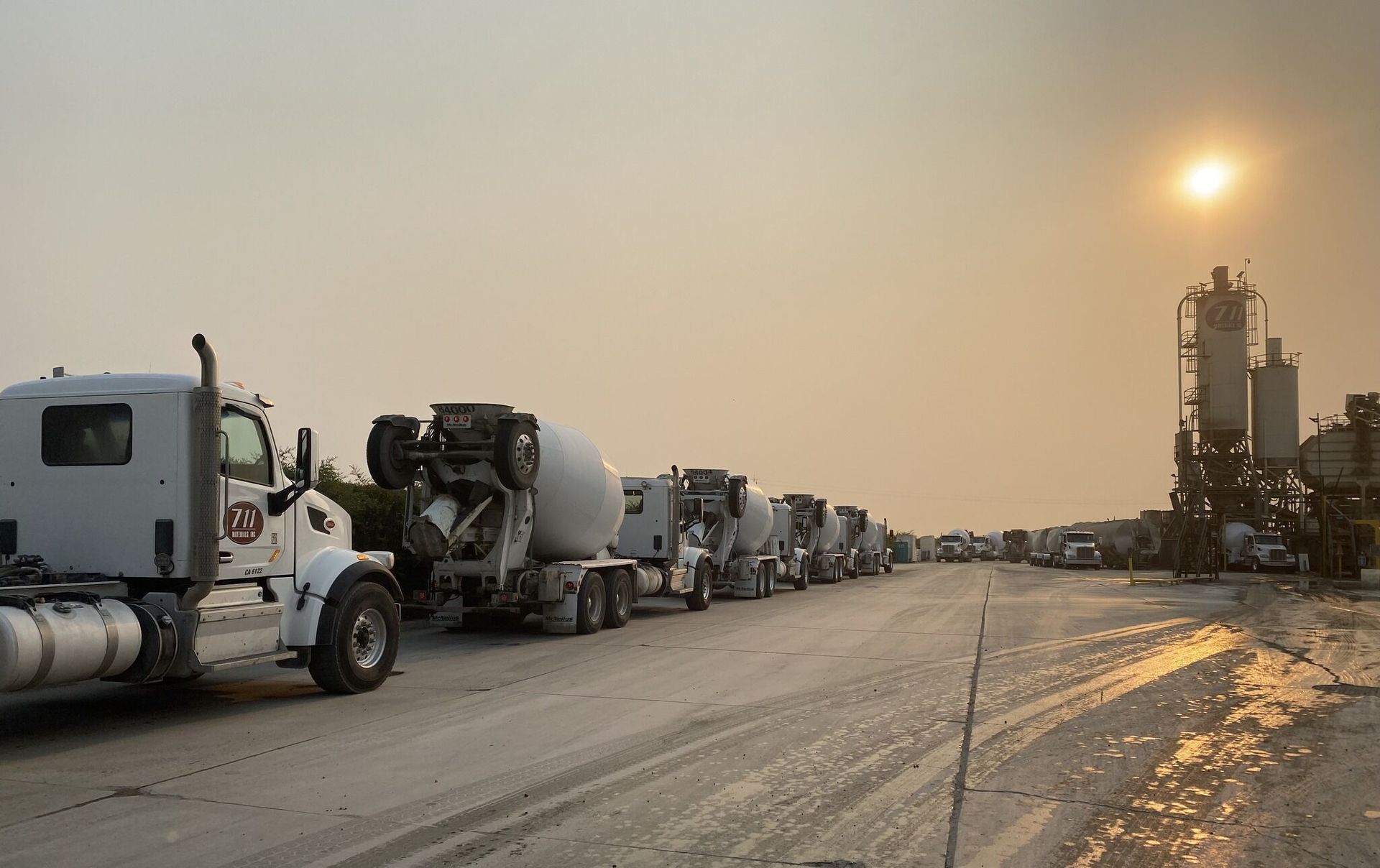 A row of cement trucks are parked on the side of the road.