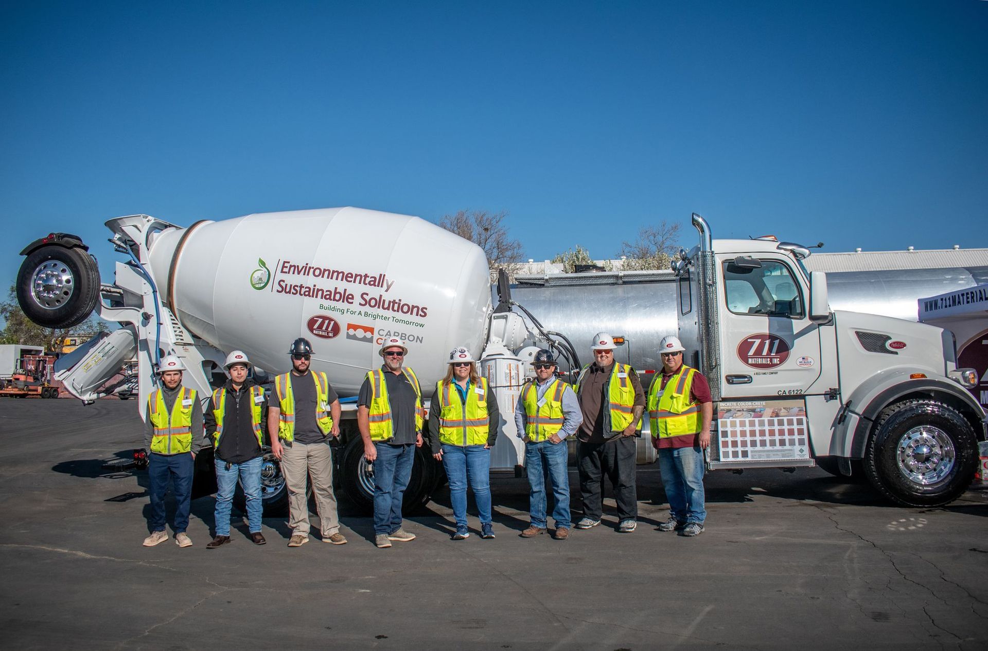 A group of construction workers are posing for a picture in front of a concrete mixer truck.