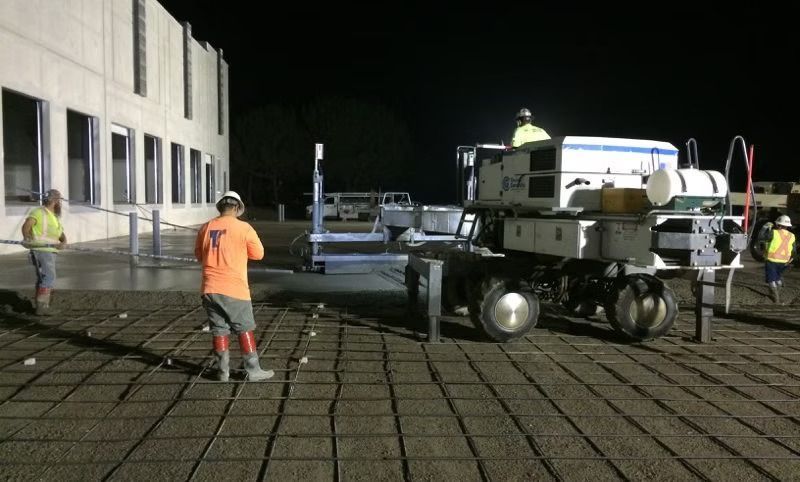 A group of construction workers are working on a concrete driveway at night.