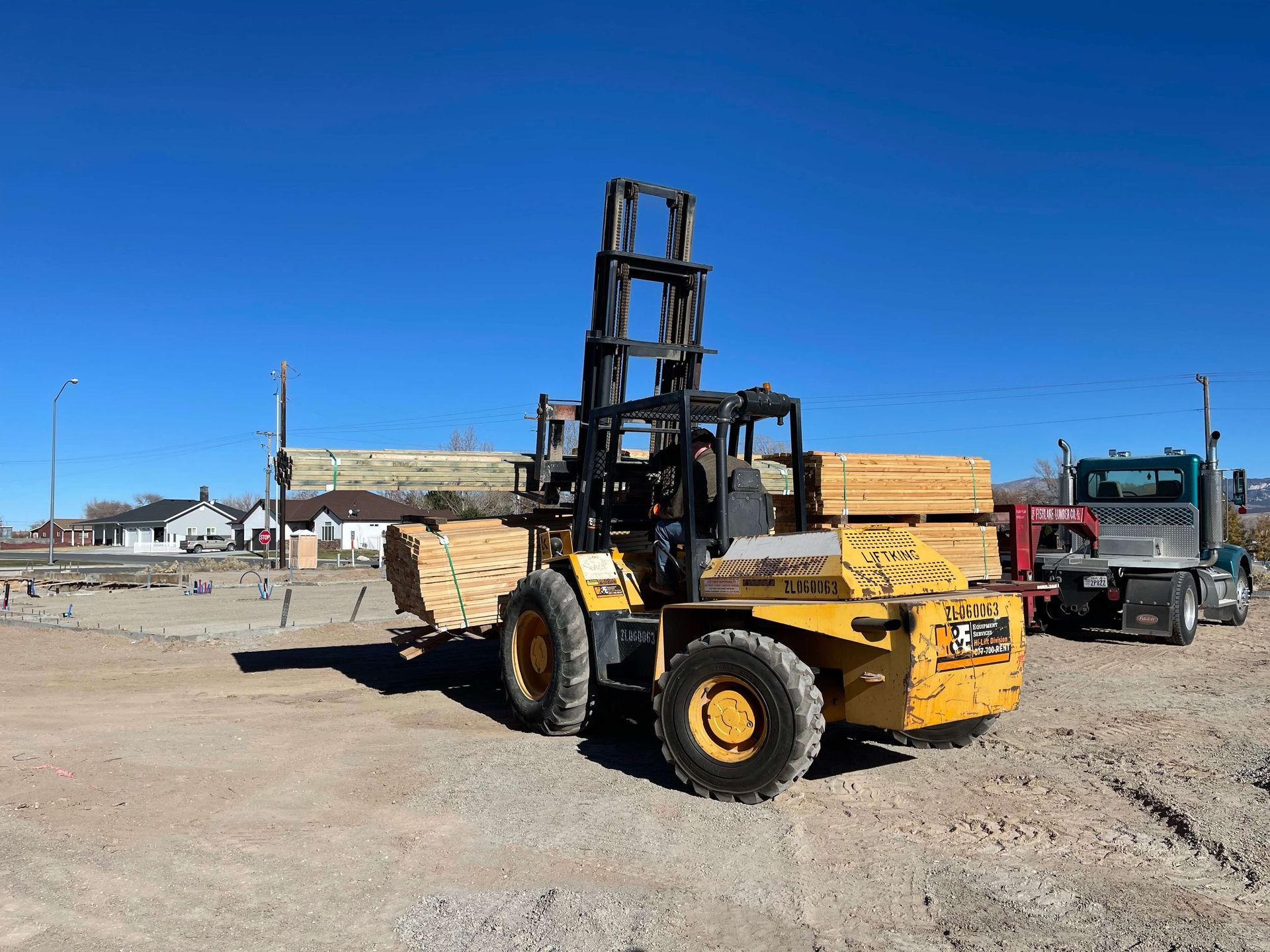 A yellow forklift is carrying wood in a dirt field.