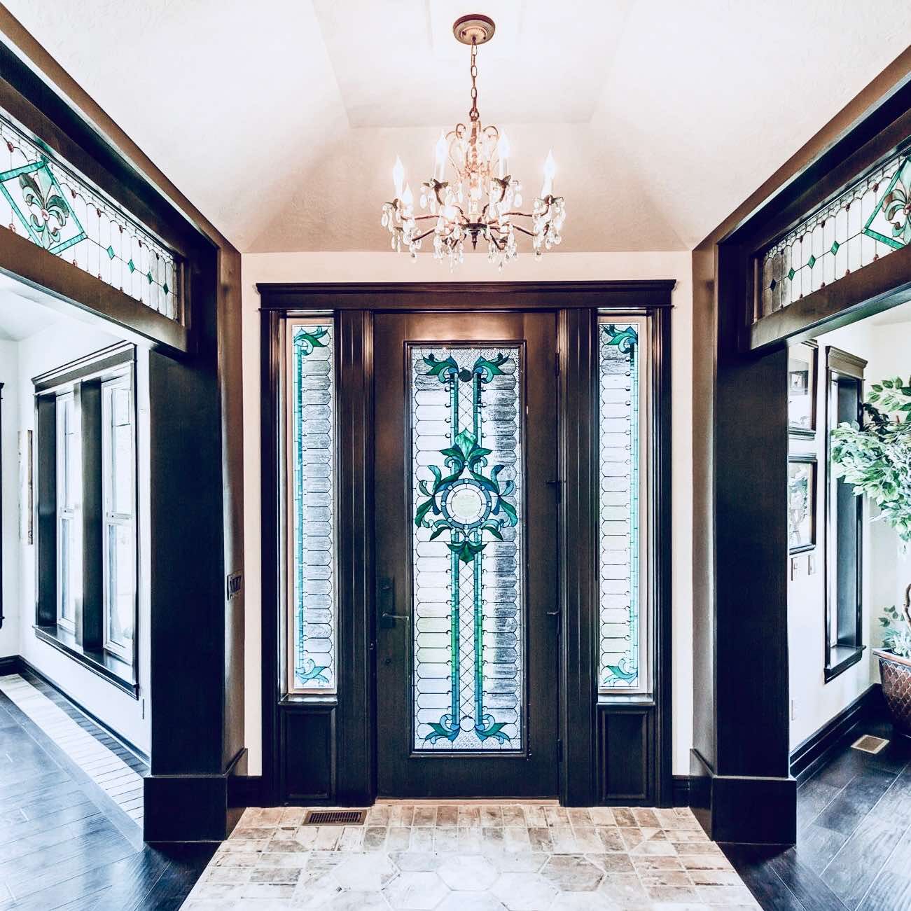 A hallway with a stained glass door and a chandelier hanging from the ceiling