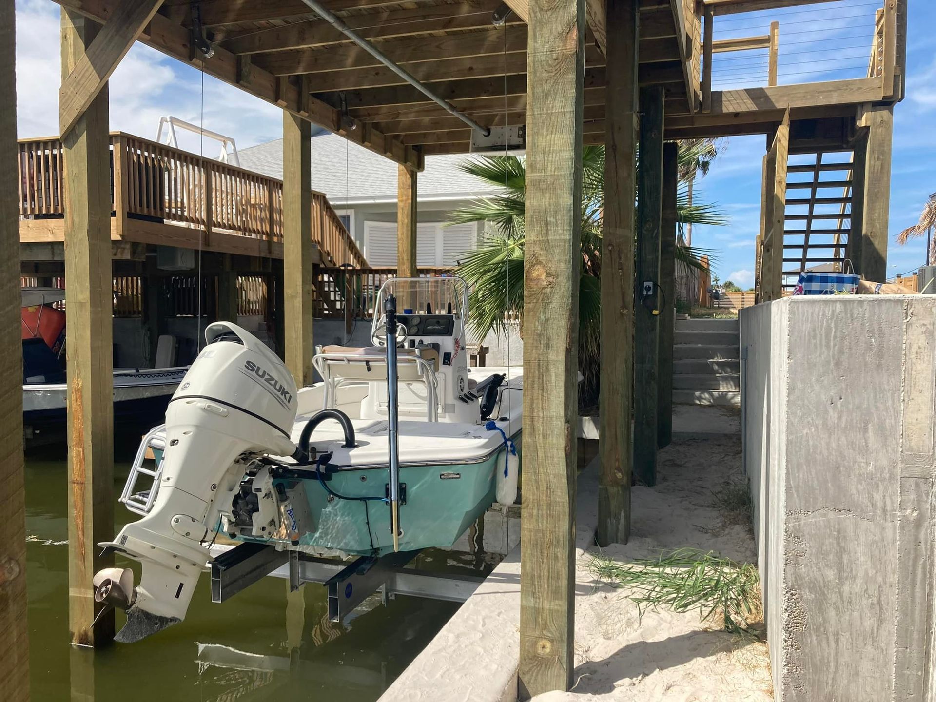 Boat under a wooden dock, near a house. Boat is light blue.