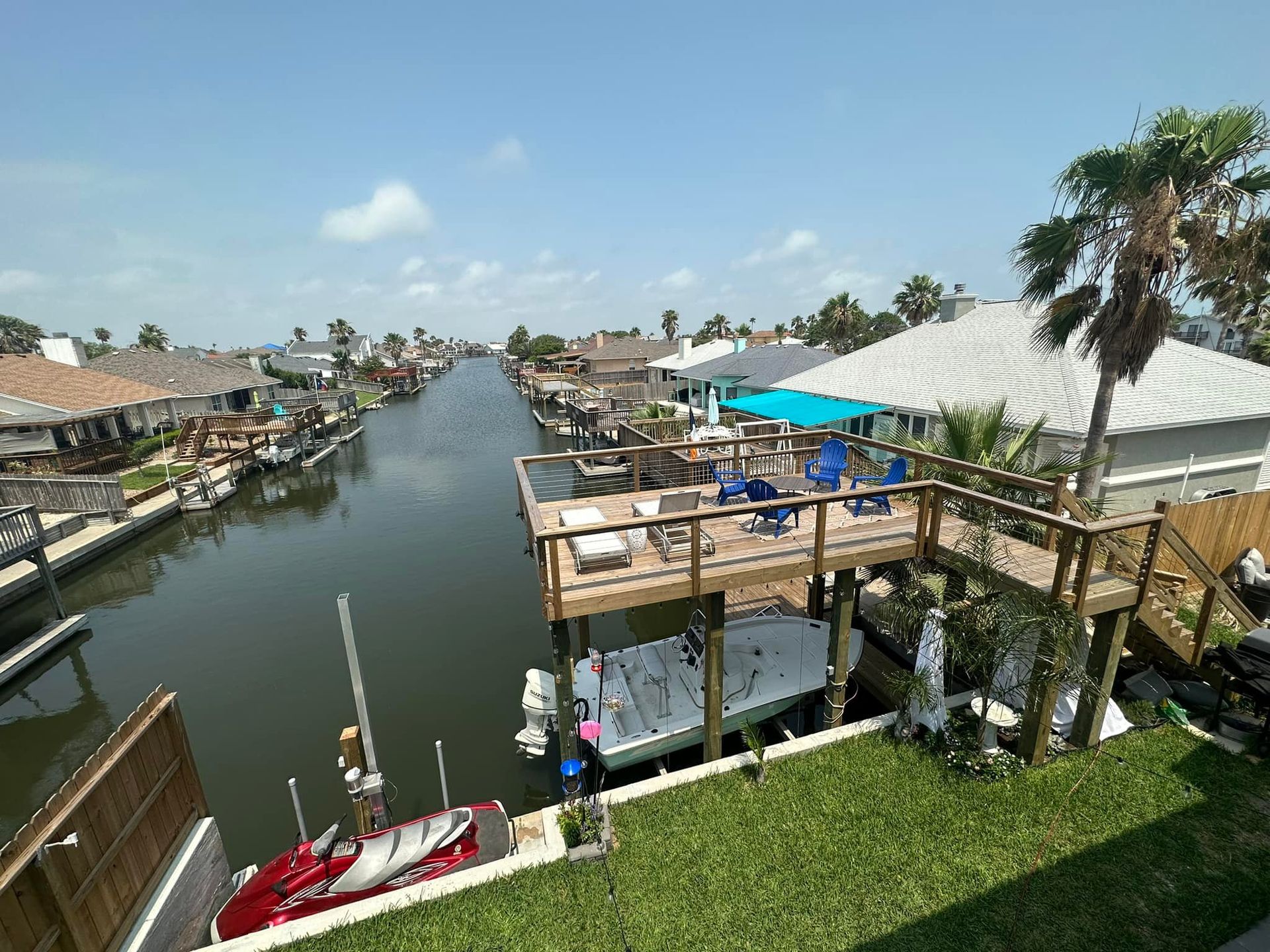 Canal with homes, boats, and a deck with blue chairs under a bright blue sky.