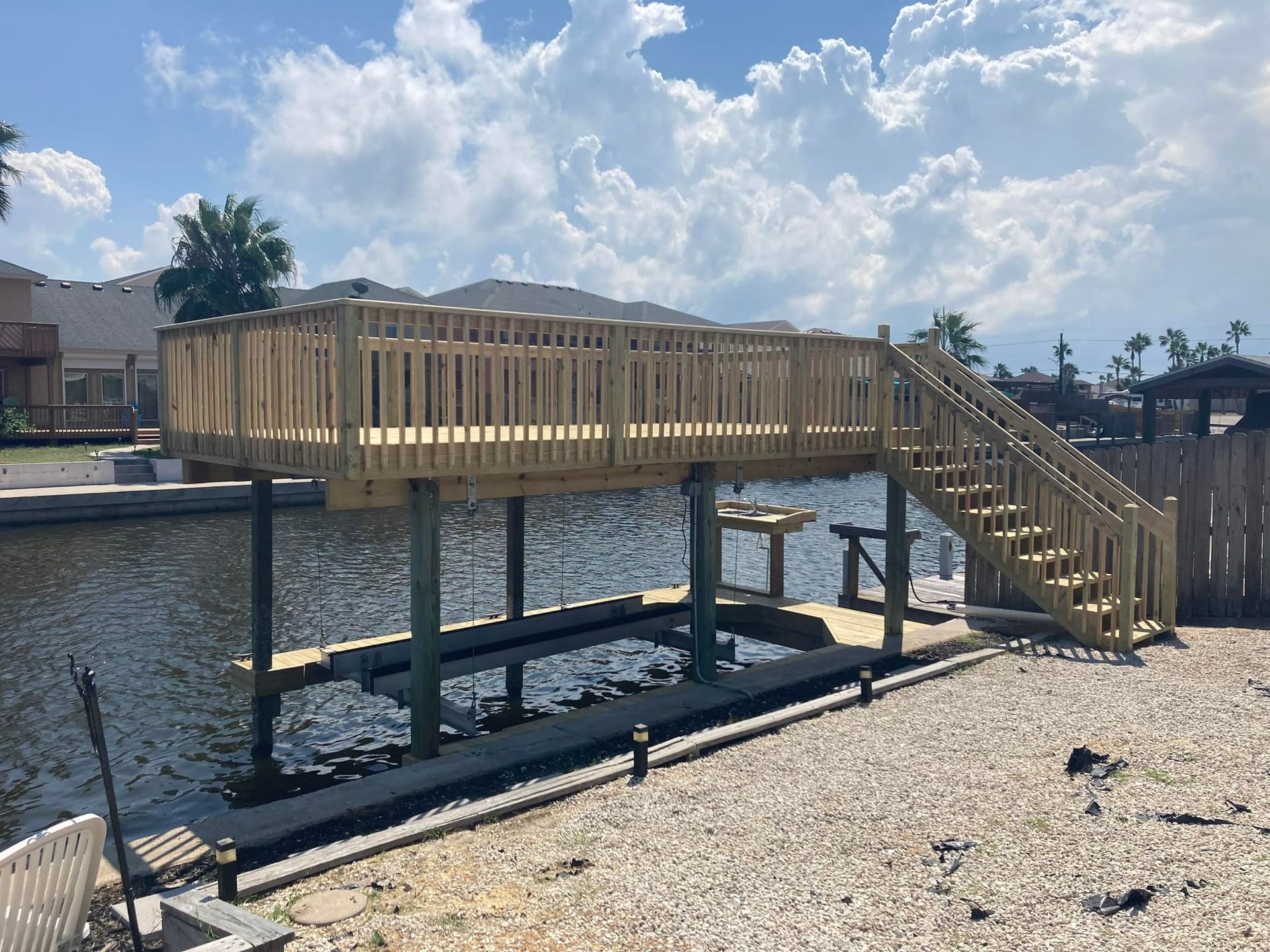 Wooden dock with elevated deck, stairs, and boat lift on a waterway, under a cloudy sky.