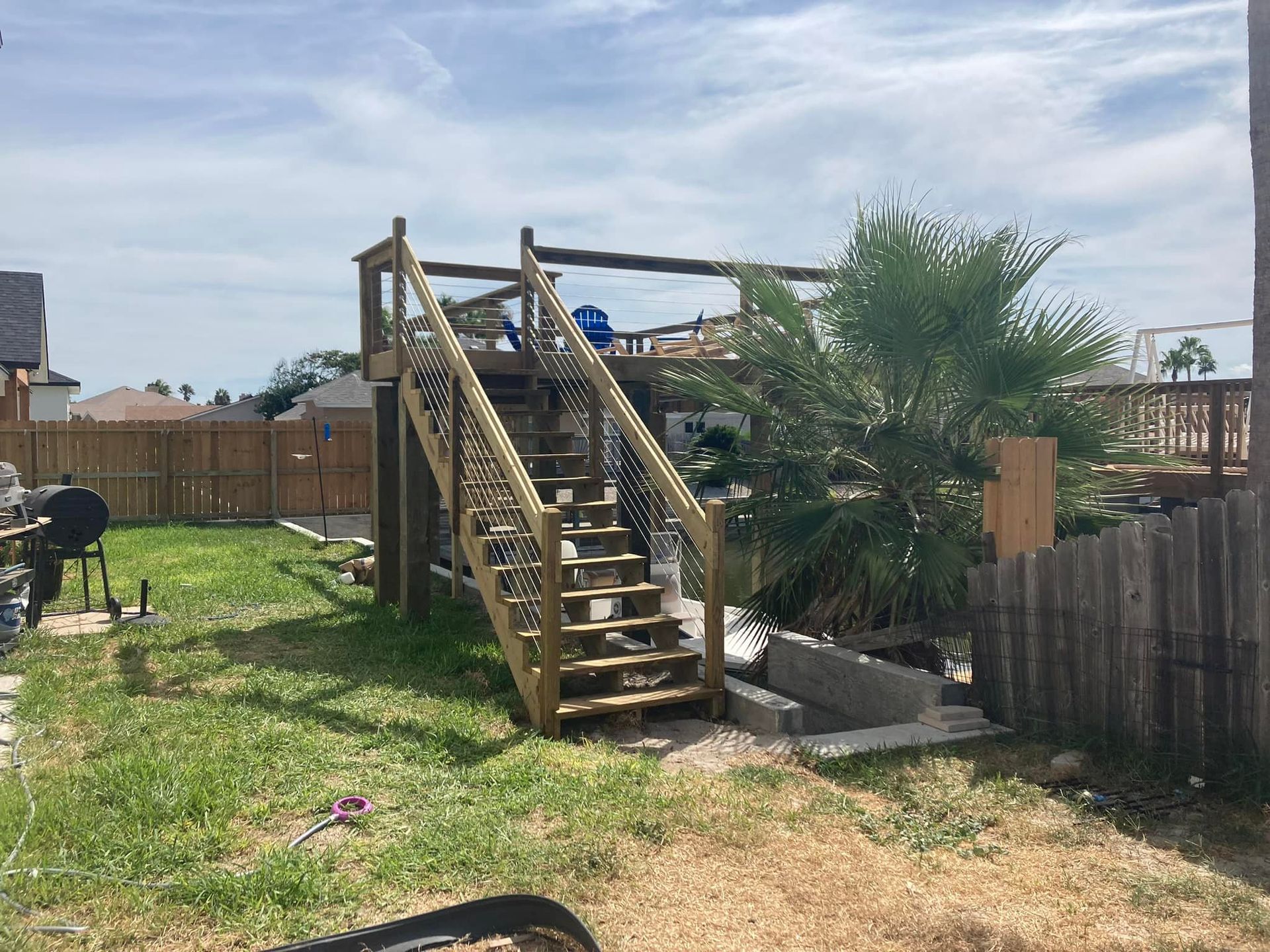 Wooden deck structure in a backyard with stairs and a palm tree.