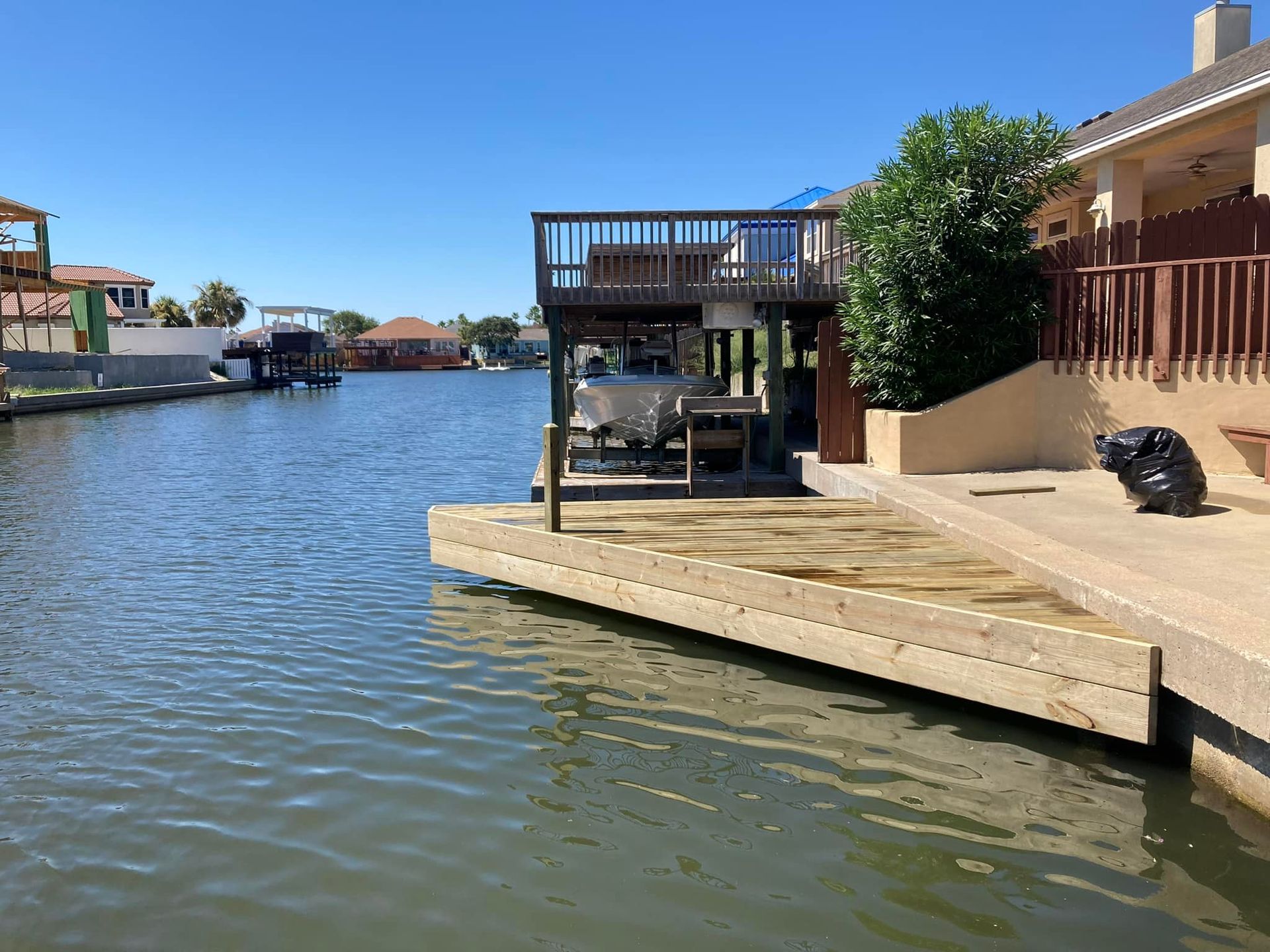 Water canal with homes and boat docks. A two-story deck with boat lift and docked boat. Clear blue sky.