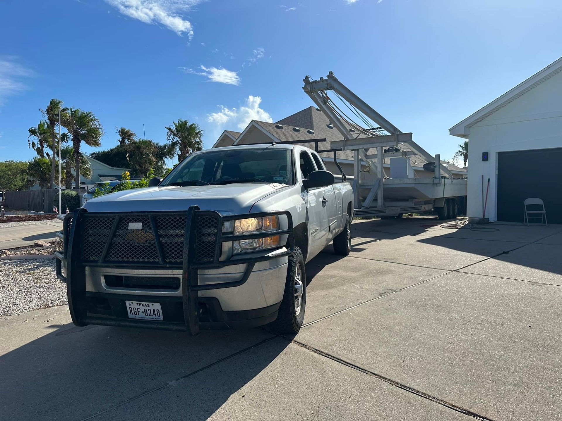 Silver truck towing large white object; parked in driveway, sunny day.