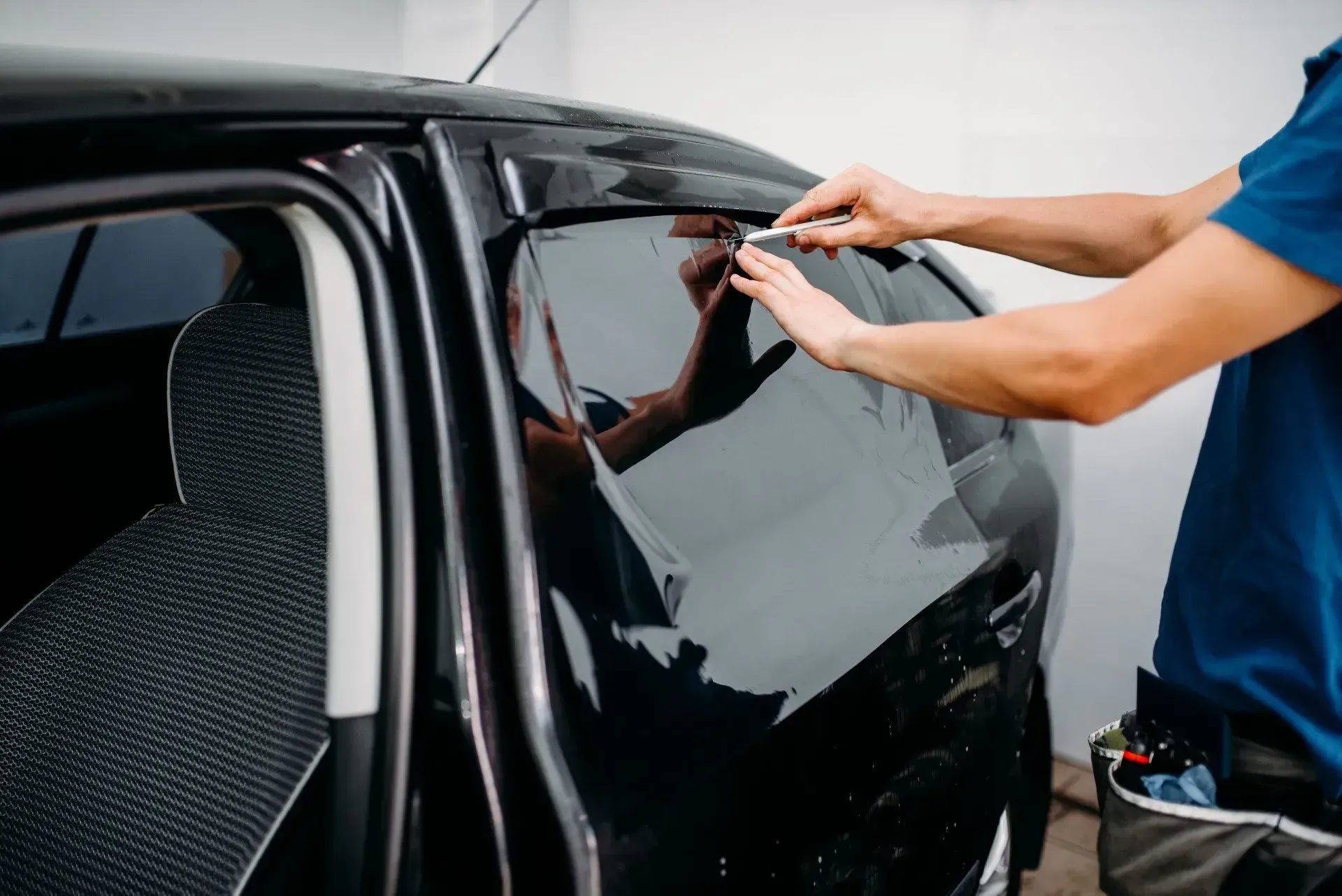 A man is applying tinted window film to a car window.