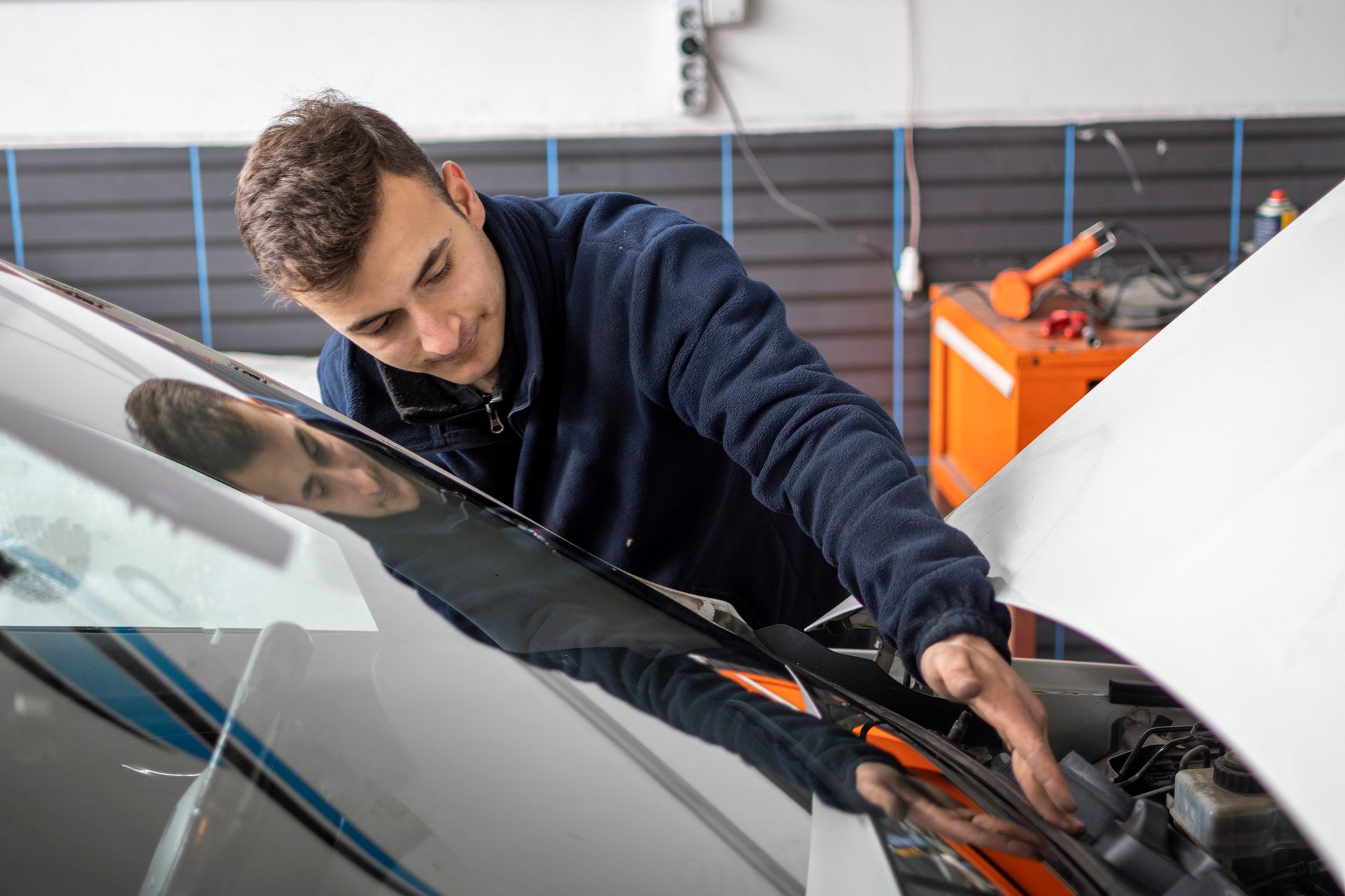 A man is working on the windshield of a car in a garage.