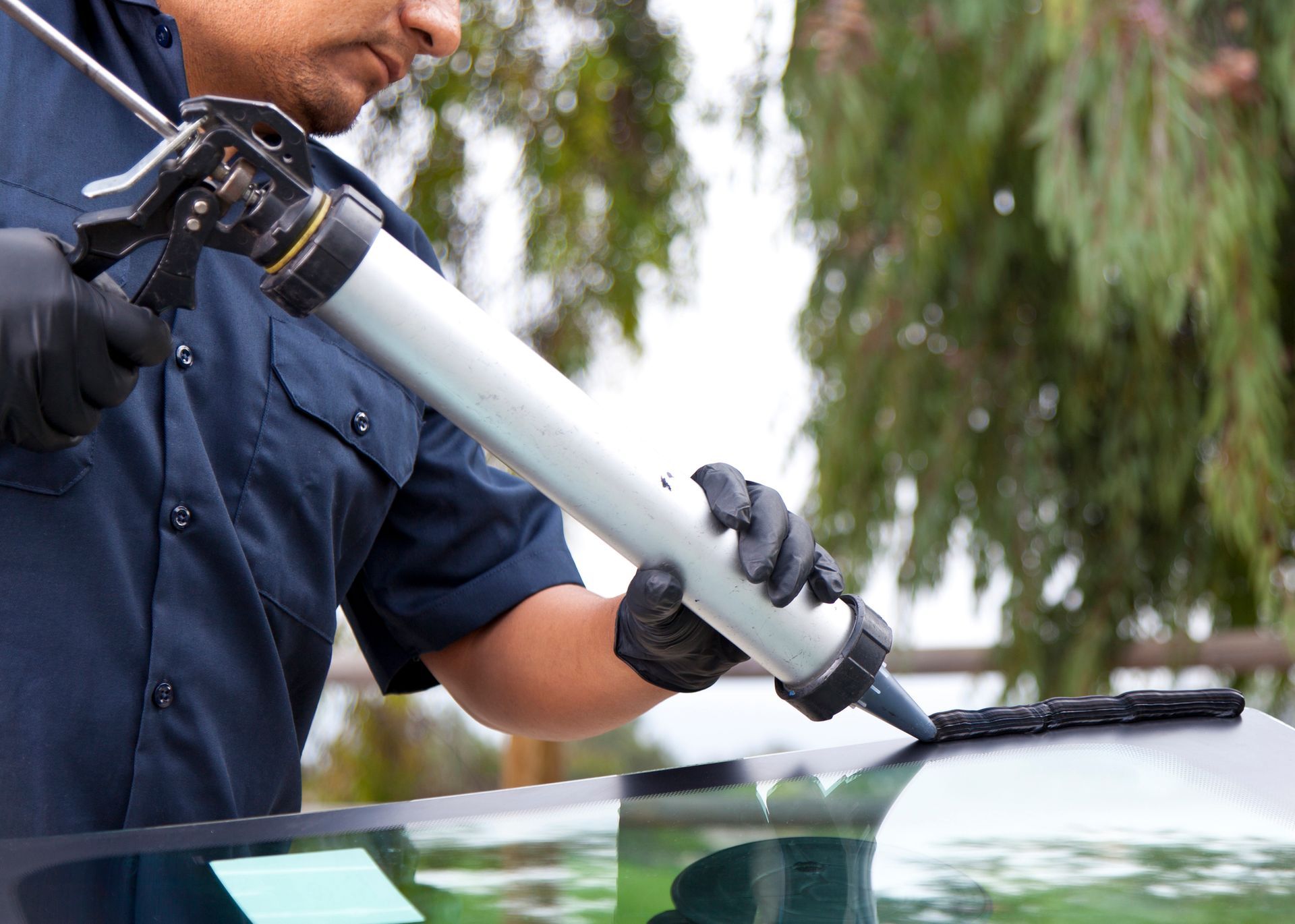 A man is applying silicone to a windshield of a car.