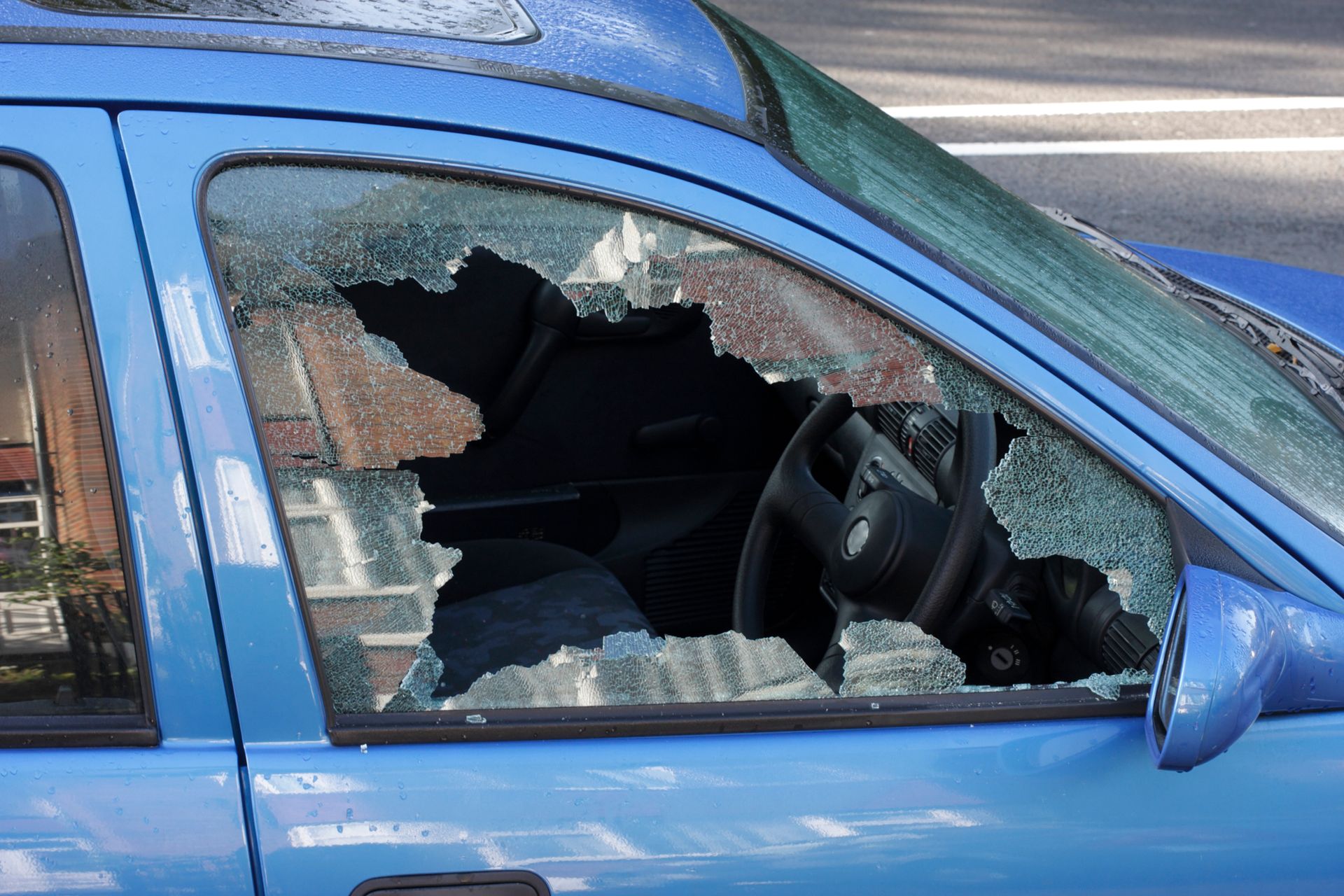 A blue car with a broken windshield is parked on the side of the road.