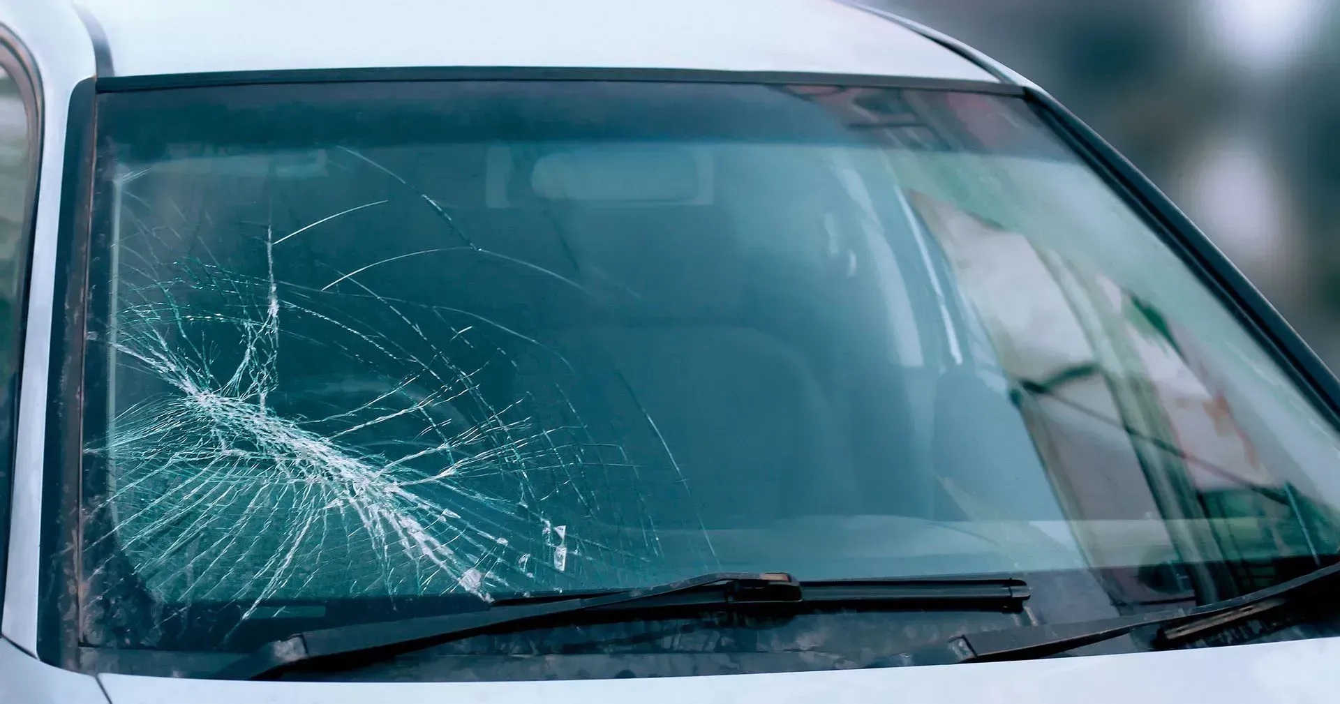 A white car with a broken windshield is parked in a parking lot.