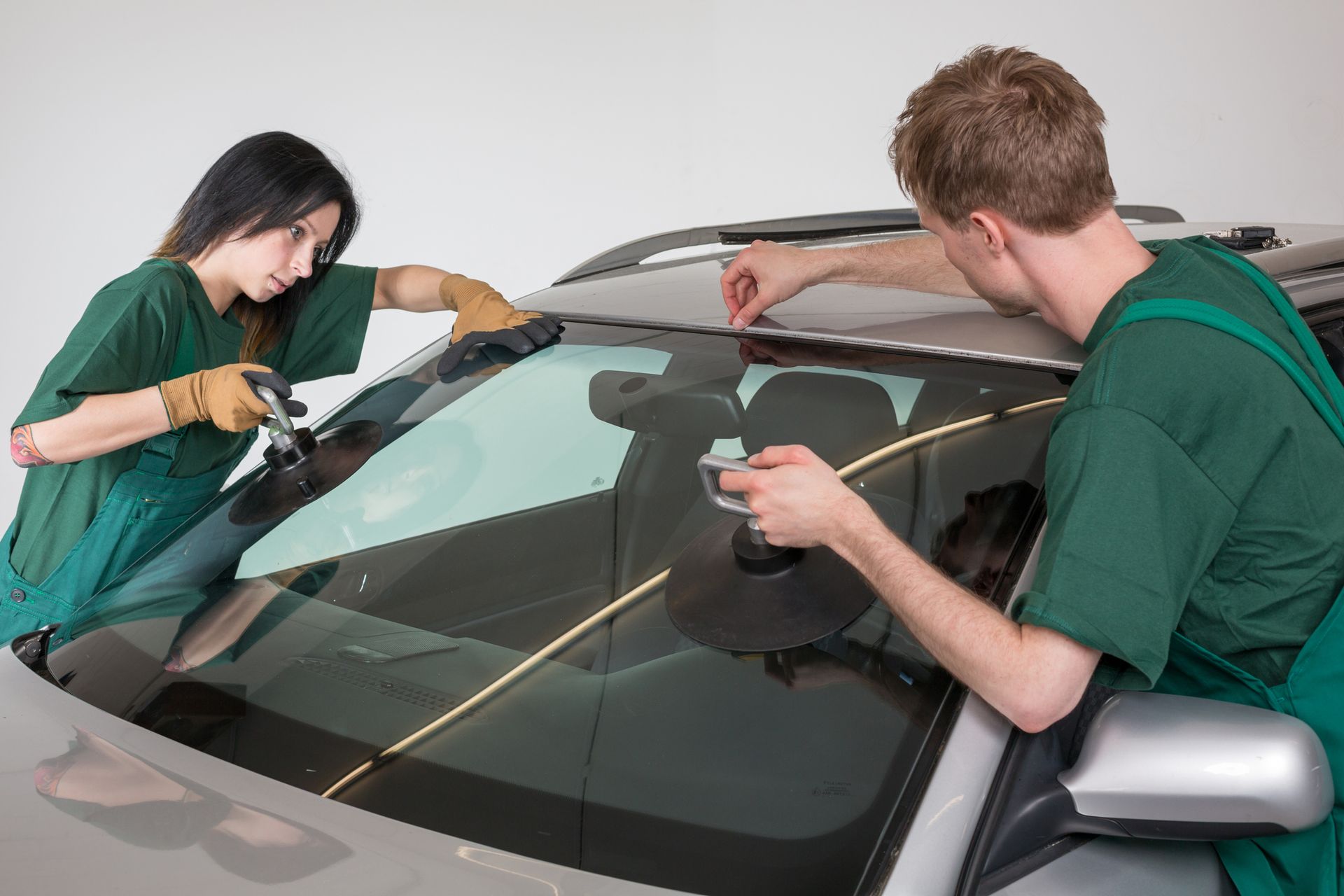 A man and a woman are working on a car windshield.