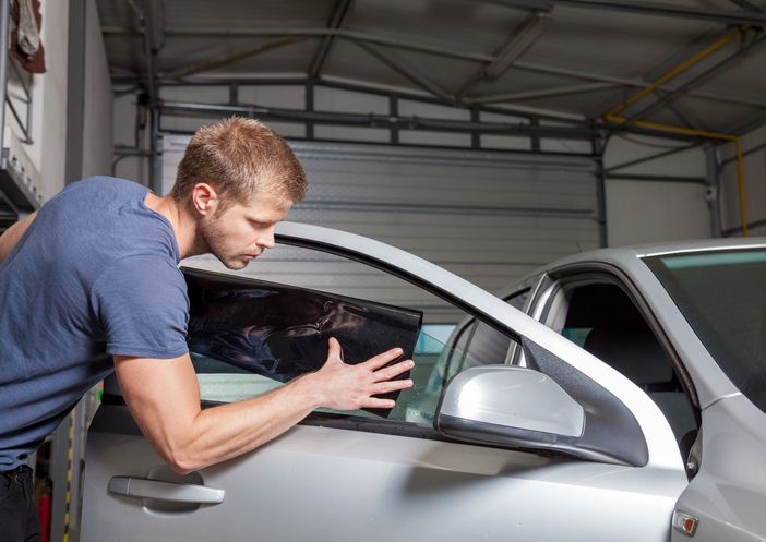 A man is applying tinted glass to a car window.
