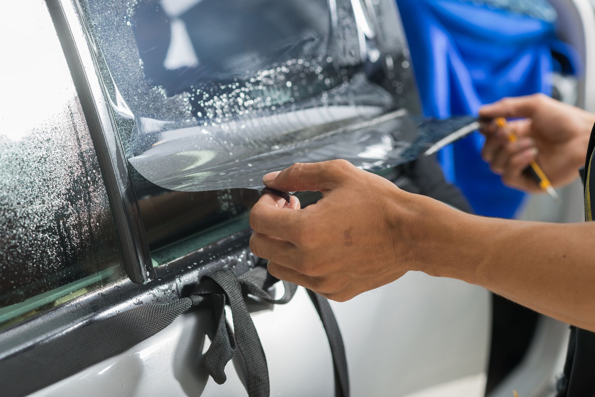 A person is applying tinted window film to a car window.
