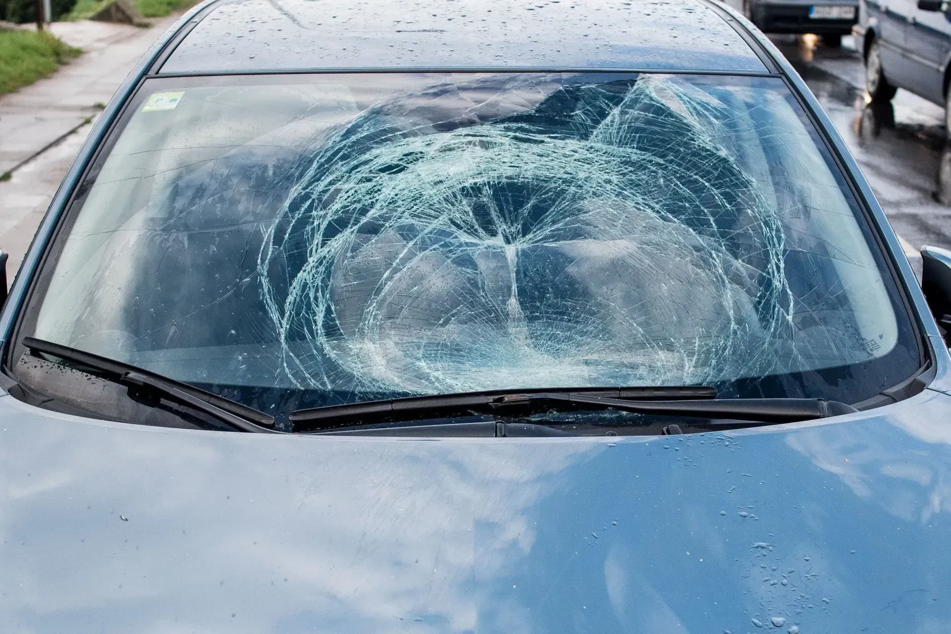 A car with a broken windshield is parked on the side of the road.