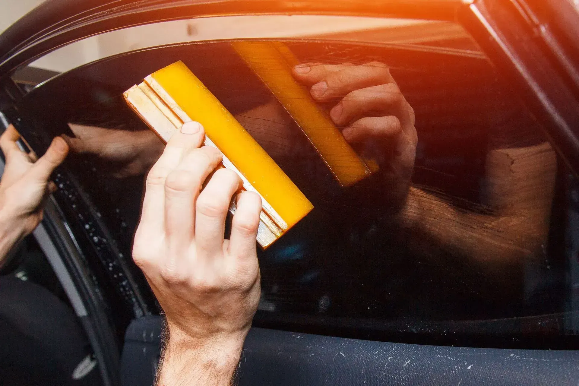 A person is applying tinted window film to a car window.