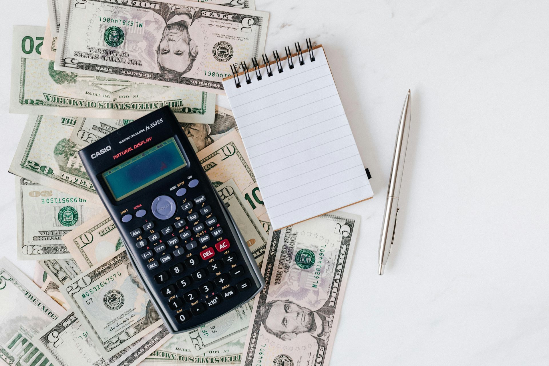 Cash, calculator, notepad, and pen on a white surface, suggesting financial planning.