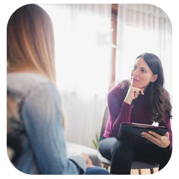 Two people in a bright room talking, one holding a tablet and taking notes.