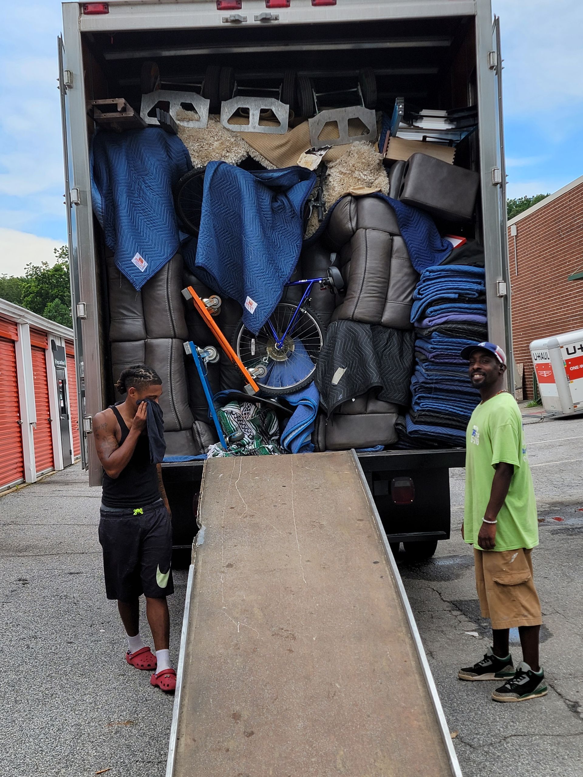 Two people loading a moving truck with furniture, ramp extended.