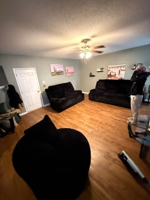 Living room with black furniture, wooden floor, and a person standing near a couch.