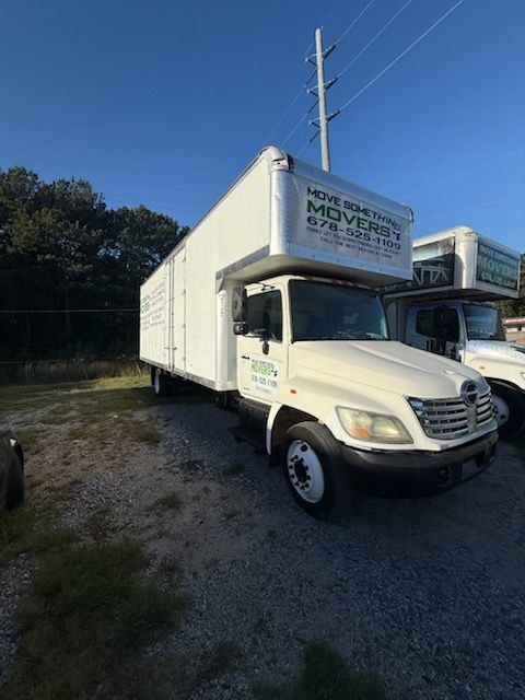 White moving truck parked outdoors under a blue sky, another truck is visible in the background.